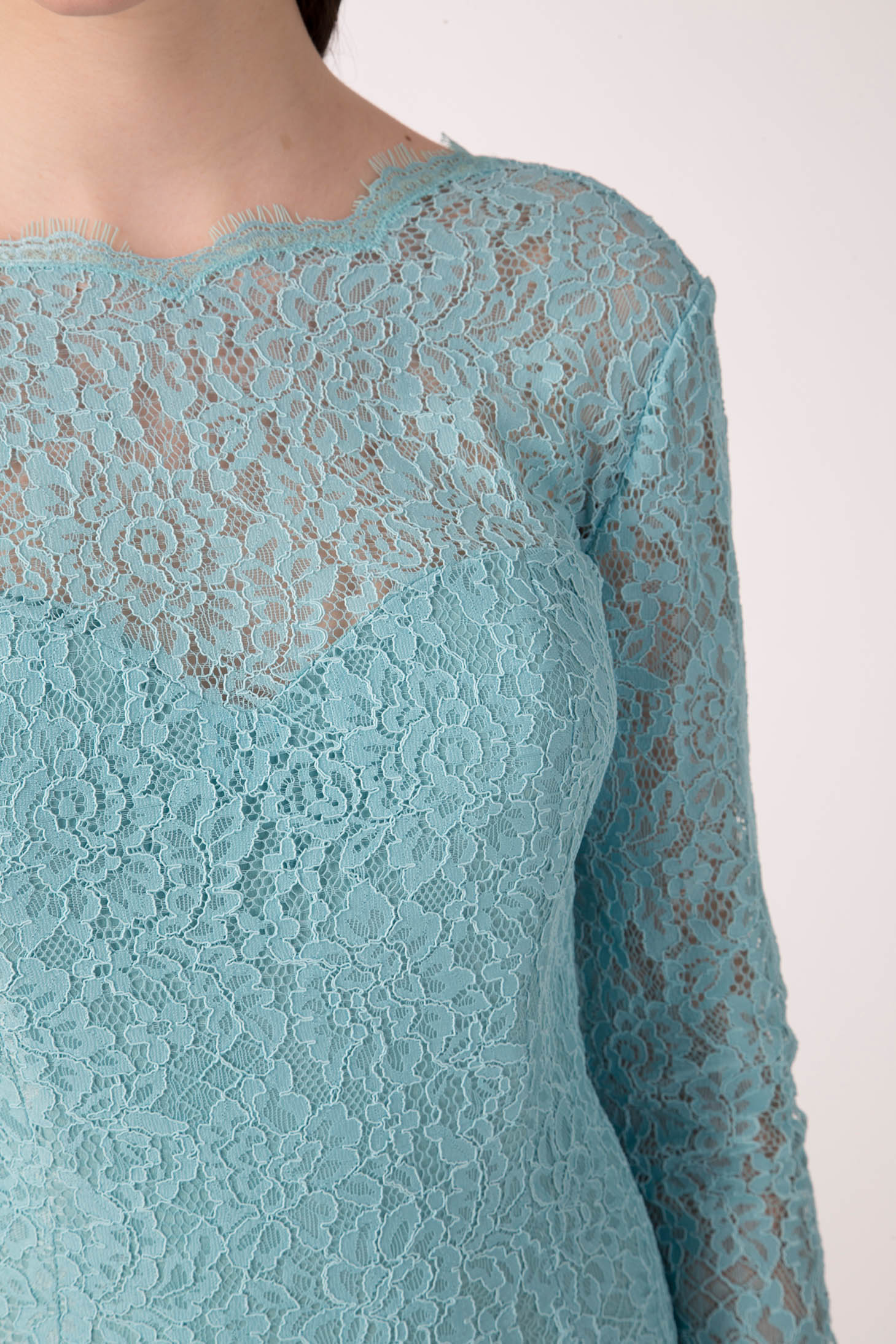 A close-up of a person wearing the Antonio Croce Ambeta Long-Sleeve Lace Dress evokes an elegant look with its light blue lace and floral patterns. This vintage piece from Antonio Croce features long sleeves and a scalloped neckline, set against a plain, neutral background.