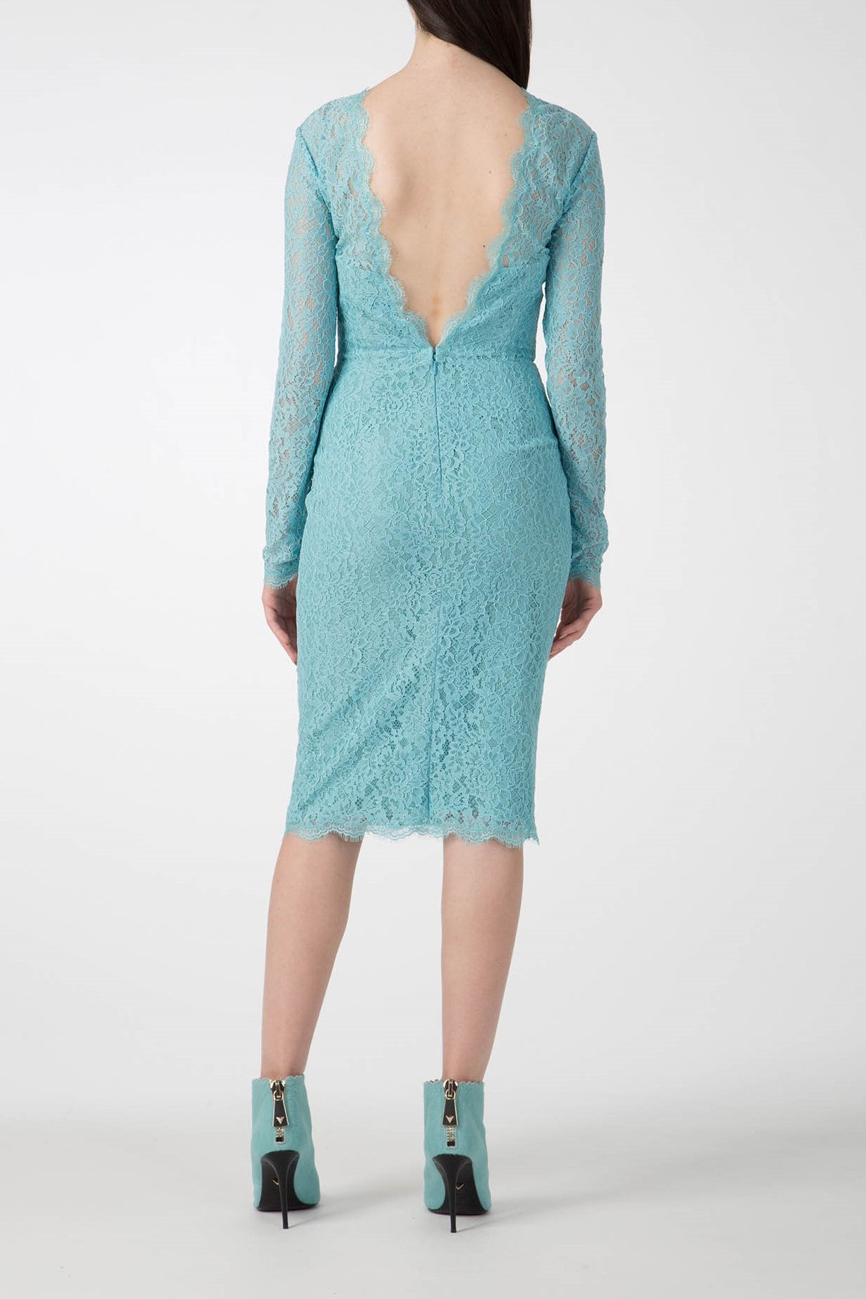 A woman models a vintage piece with the Antonio Croce Ambeta Long-Sleeve Lace Dress, showcasing its teal color, deep V back, knee-length cut, and long sleeves. Complementing her elegant look are matching teal ankle boots with heels. The scene is set against a plain white background.