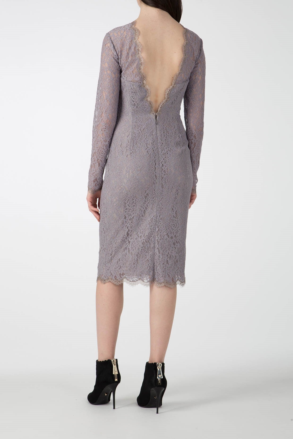 A rear view of a person showcases the Antonio Croce Ambeta Long-Sleeve Lace Dress, a vintage piece with knee-length, light purple lace and a deep V-back. The elegant look is complemented by black ankle boots with zippers on a plain white background.
