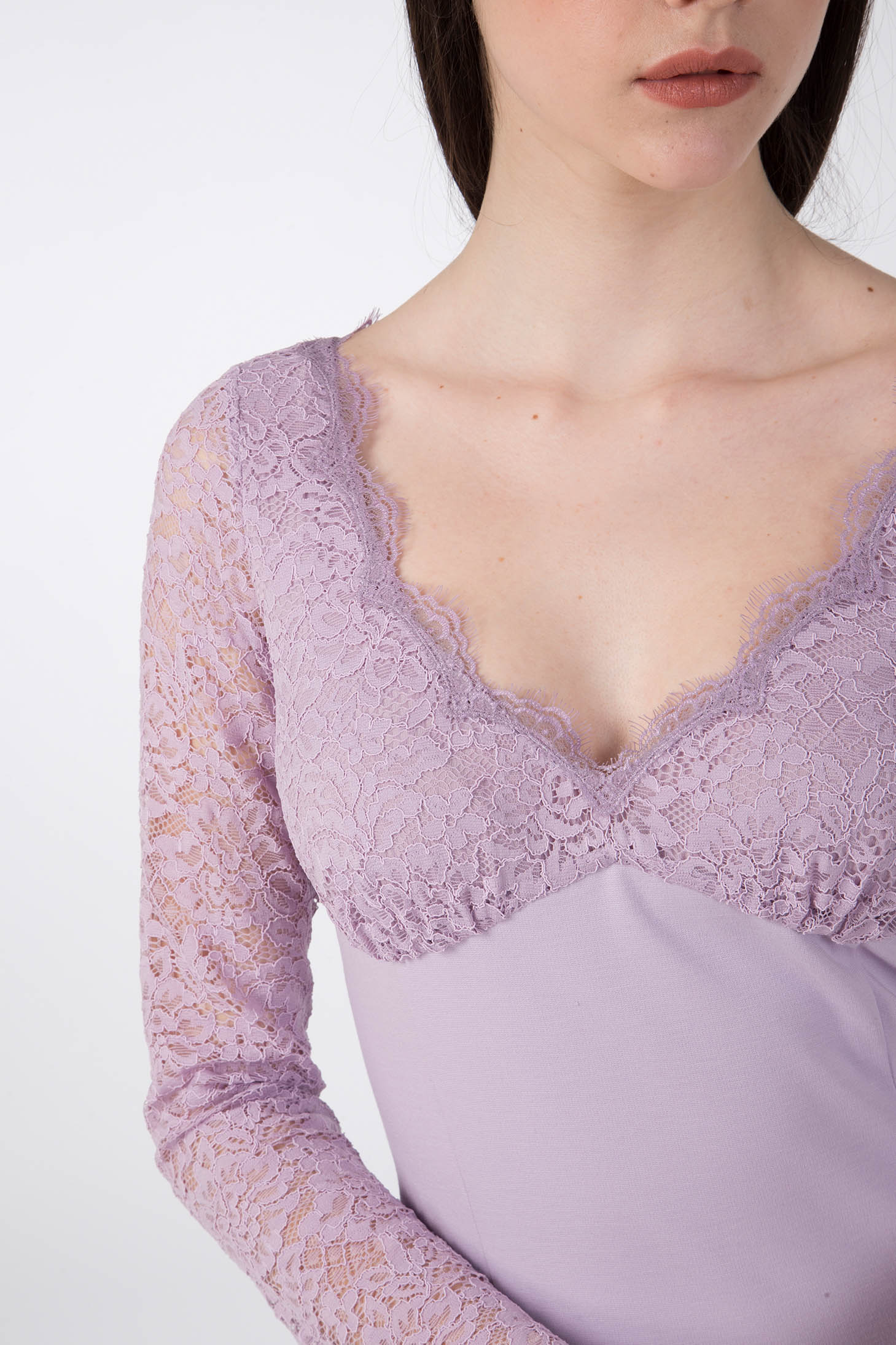 A person wearing the Antonio Croce Ampara Embroidered Lace Dress, showcasing exquisite lavender lace with long sleeves. The delicate lace fabric enhances the charm of the V-neckline and sleeves, set against a plain light-colored background.
