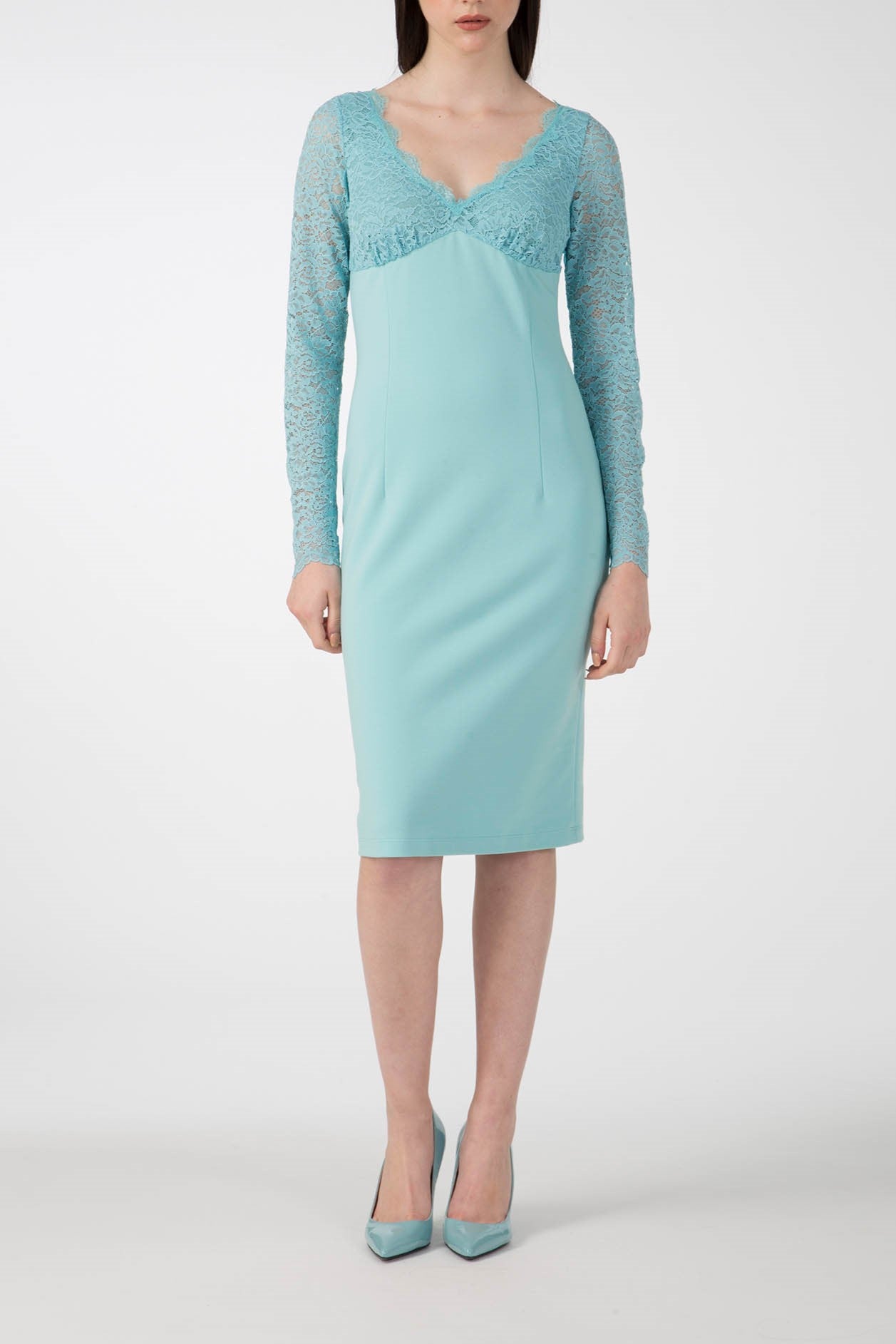 A woman is dressed in the Antonio Croce Ampara Embroidered Lace Dress, showcasing its elegance with intricate embroidery on the lace sleeves and a sweetheart neckline. She pairs it with matching teal high heels against a plain white background.