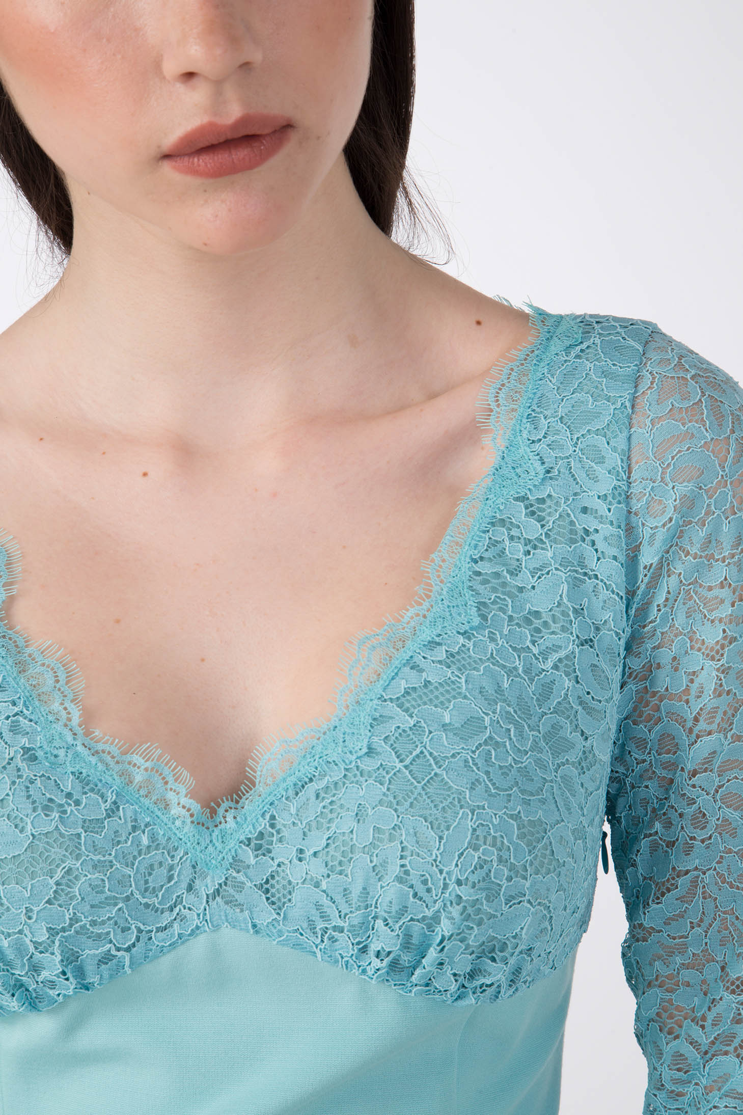 The person is wearing the Antonio Croce Ampara Embroidered Lace Dress in light blue, visible from the shoulders to mid-torso. This elegant dress by Antonio Croce features a low V-neckline and delicate lace fabric with intricate patterns on the sleeves and chest area. The background is plain white.