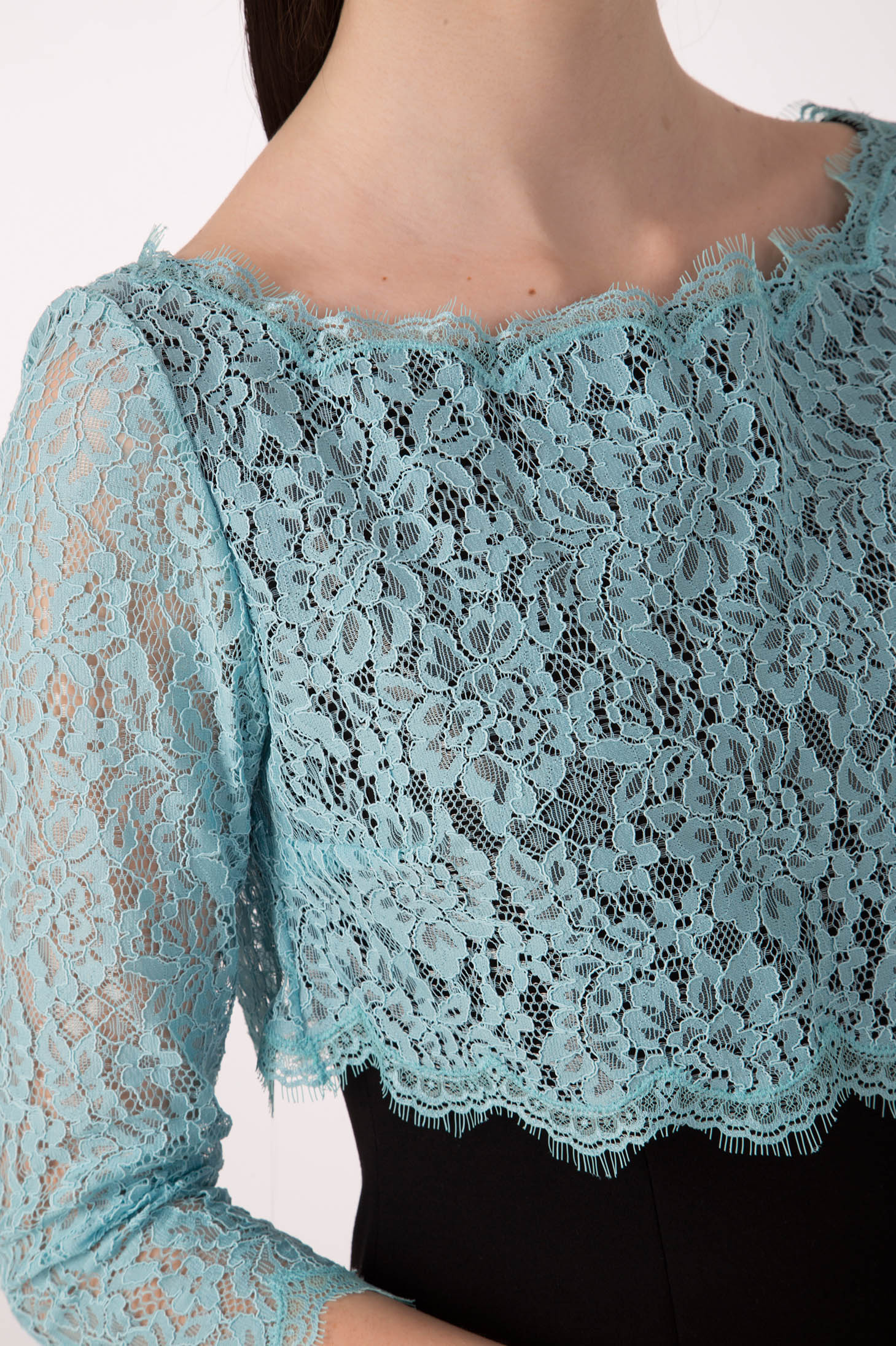 A woman is seen modeling the Antonio Croce Artemide Two-Tone Dress, featuring an intricate aqua lace bodice with three-quarter sleeves over a sophisticated black dress. The floral pattern of the lace adds a delicate and elegant touch, while its A-line silhouette embodies timeless grace against a plain background.