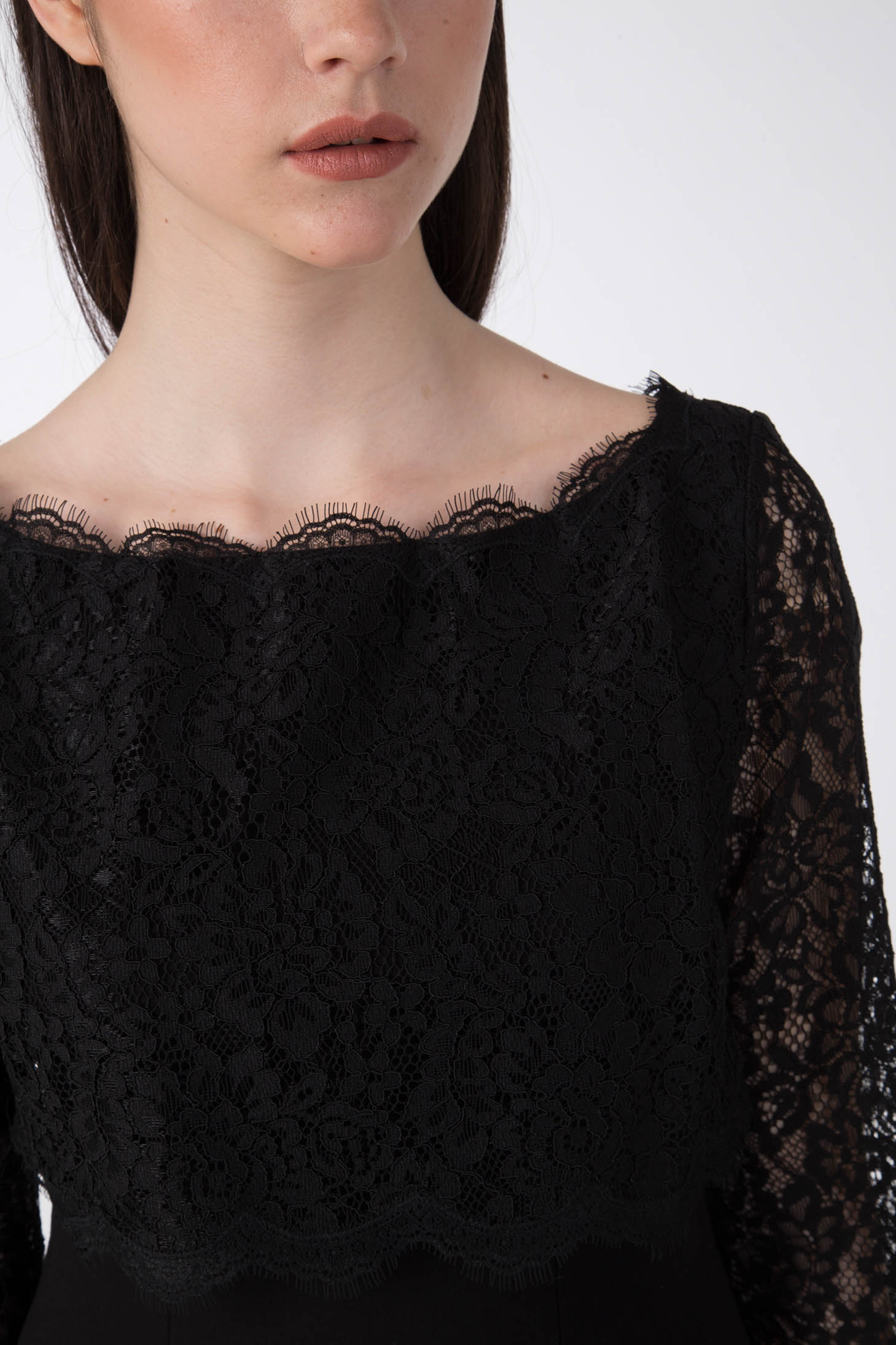 A woman is wearing the sophisticated Antonio Croce Artemide Two-Tone Dress, featuring an elegant A-line silhouette. Only her lower face and upper body are visible. The dress showcases intricate lace patterns, a delicate neckline, and long lace sleeves against a plain light-colored background.