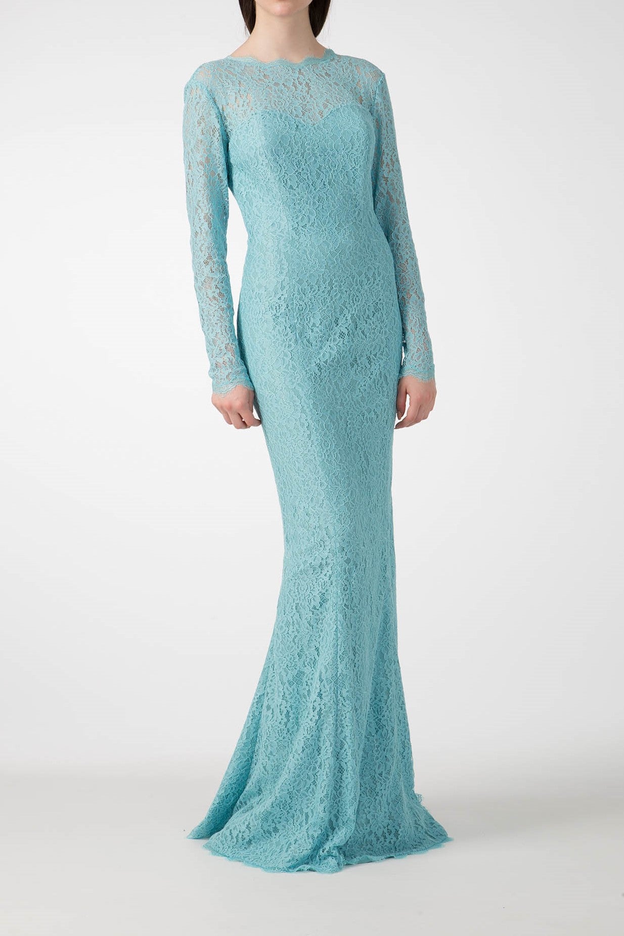 A person wearing the Antonio Croce Australia Allover Lace Gown with long sleeves. This vintage piece, by Antonio Croce, is turquoise and form-fitting, featuring a delicate illusion neckline and an intricate pattern. The background is plain white.