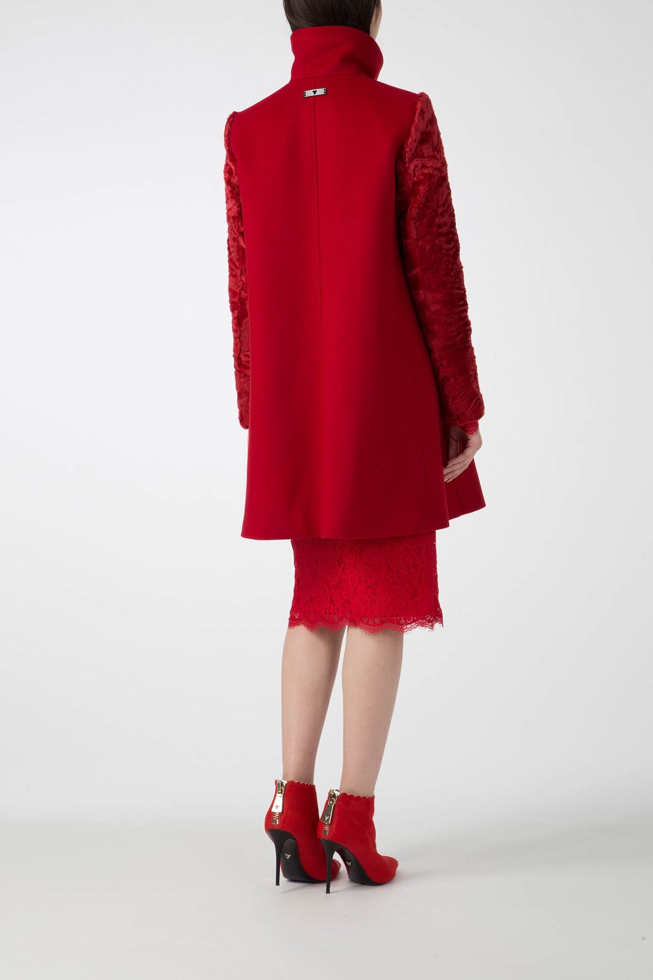 A person is wearing the Antonio Croce Callie Textured Coat with Contrast Sleeves in a vintage red, paired with a matching lace skirt. They are also sporting red high-heeled ankle boots. The plain white background accentuates the stylish ensemble as they face away from the camera.
