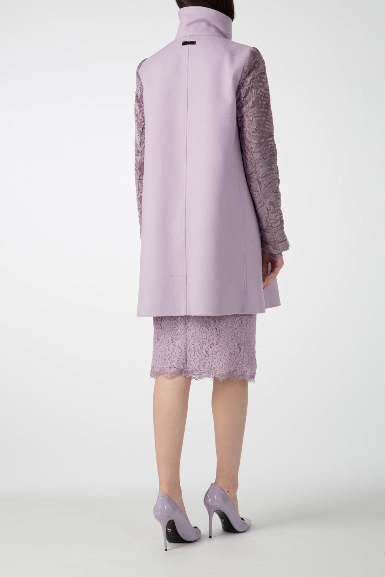 A person stands facing away, donning the Antonio Croce Callie Textured Coat with Contrast Sleeves, a stylish light purple piece with unique sleeve detail, over a lace skirt. They complement the look with matching light purple high heels. The plain white background accentuates the elegance of this vintage ensemble from Antonio Croce.