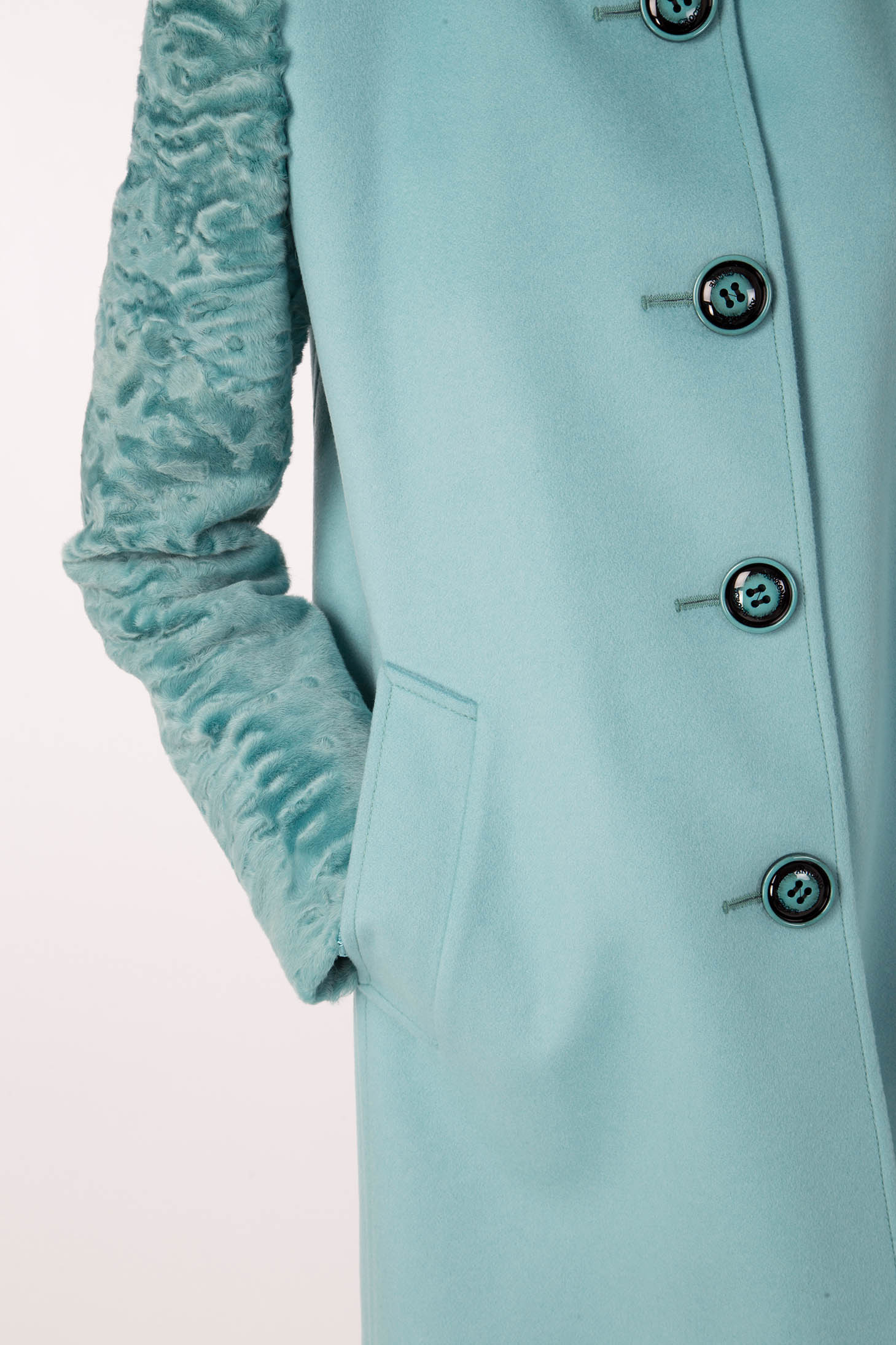Close-up of the Antonio Croce Callie Textured Coat with Contrast Sleeves in a stylish teal. This vintage-inspired piece by Antonio Croce features large black buttons and a pocket on the right side, with one arm casually tucked in. The simple white background highlights its elegant charm.