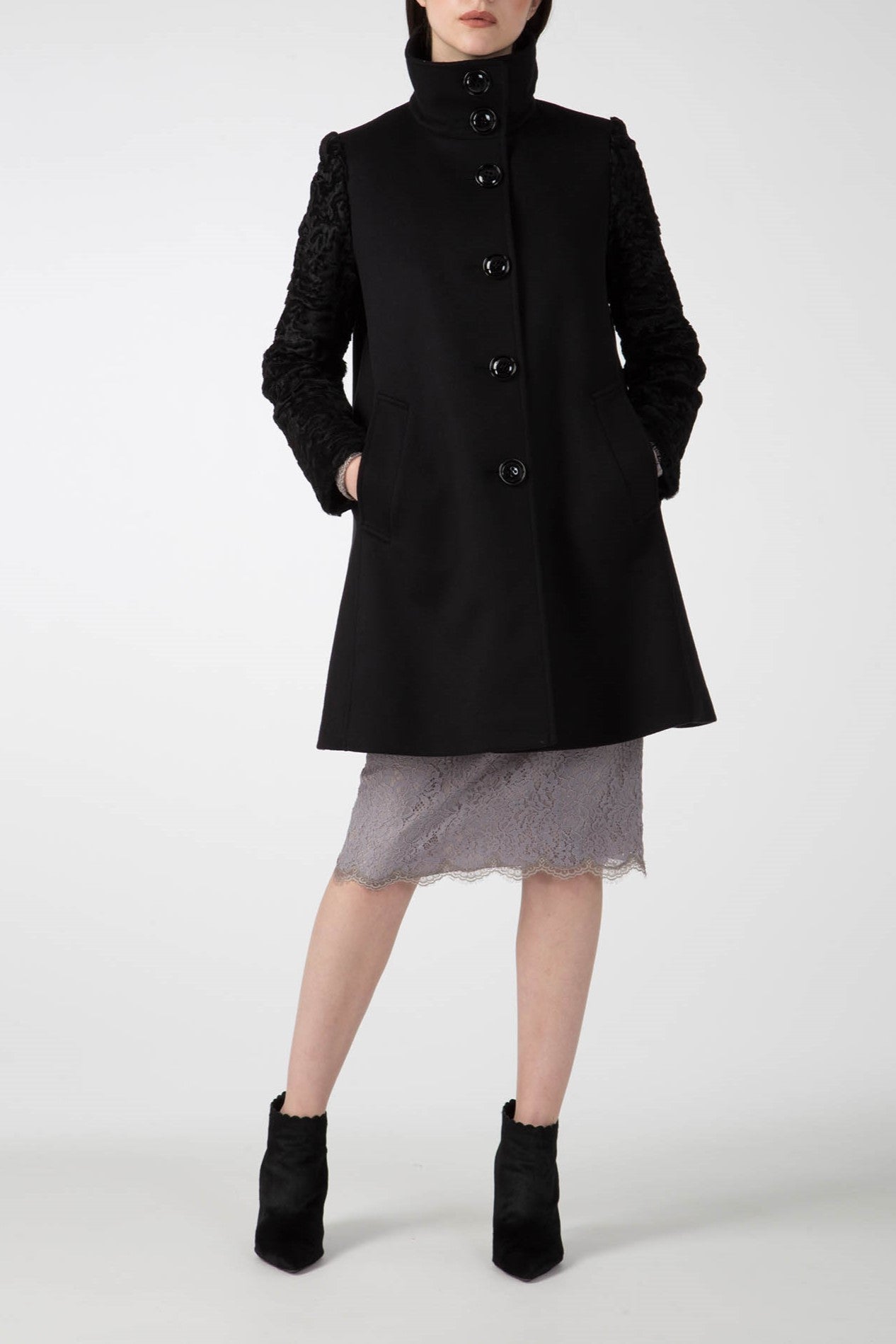 A person models the Antonio Croce Callie Textured Coat featuring contrast sleeves and button closure, paired with a gray lace skirt and black ankle boots. The plain white background highlights the ensemble's elegance.