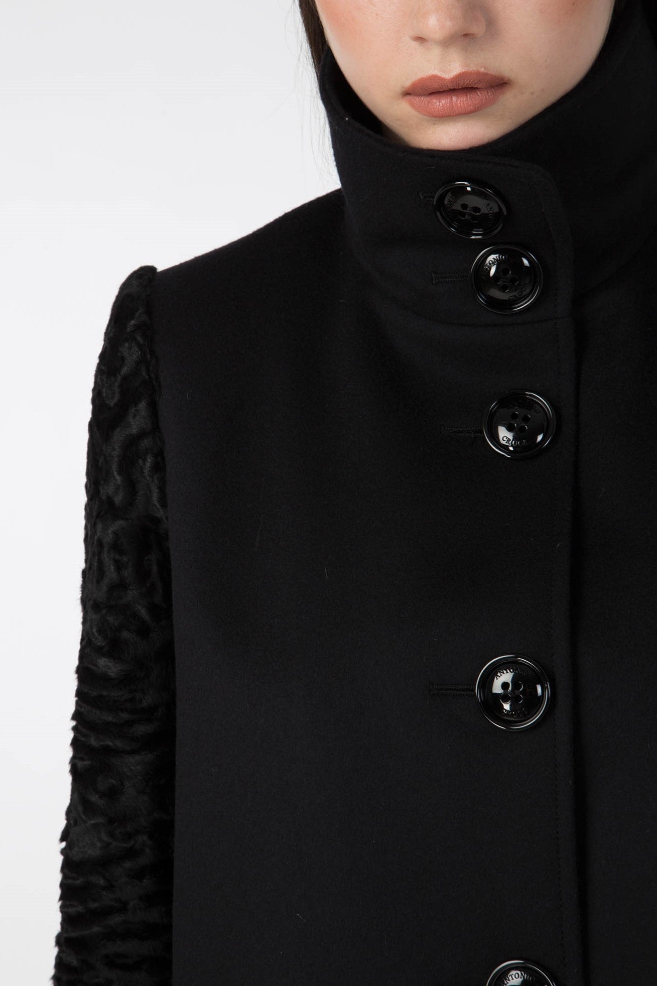 A person is wearing the Antonio Croce Callie Textured Coat, notable for its stylish high-collar and distinct sleeve design. The coat features prominent black buttons, and the emphasis is on the upper portion against a plain white background.