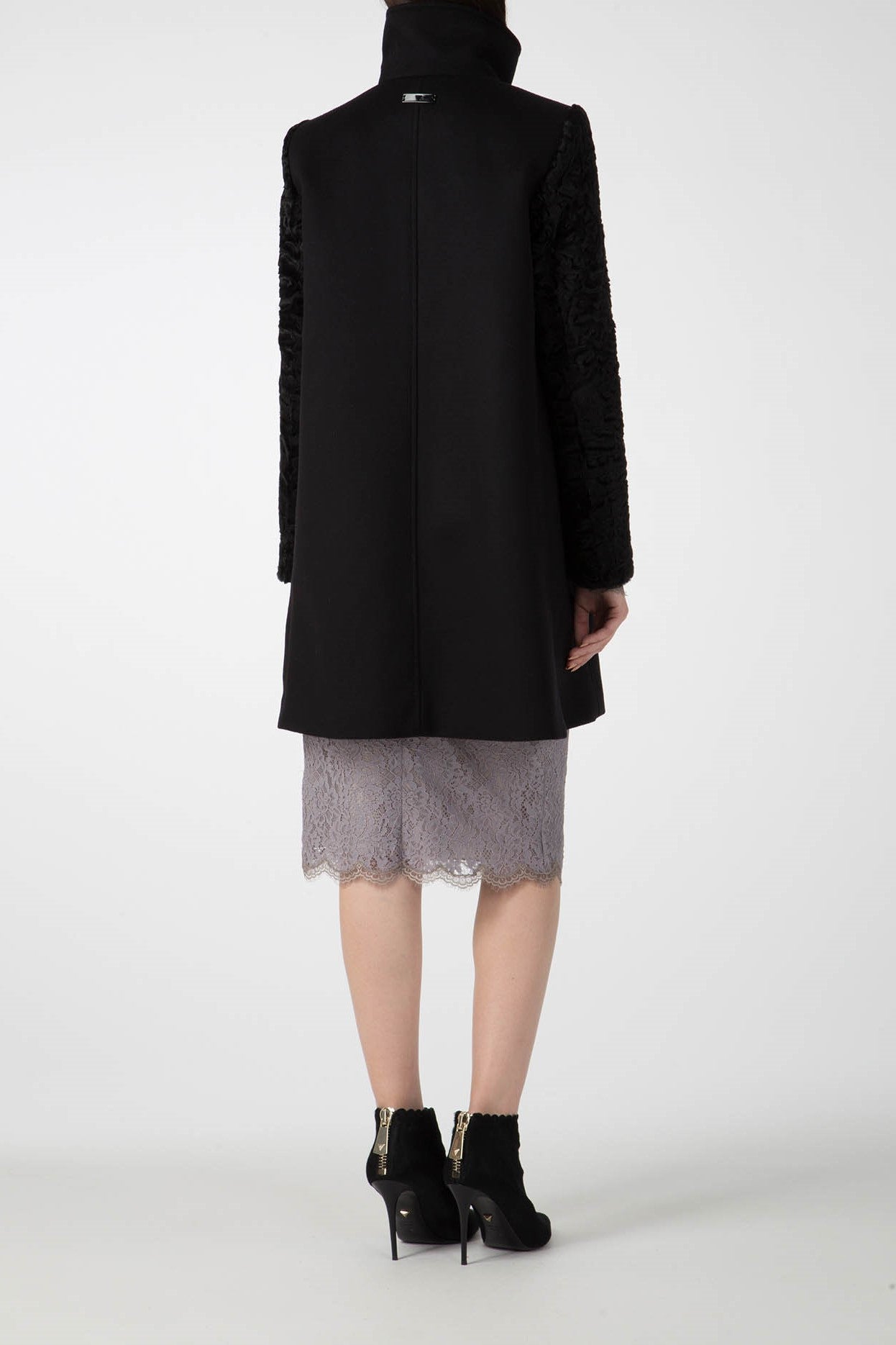 A person stands with their back turned, showcasing the Antonio Croce Callie Textured Coat with its distinctive contrast sleeves, paired perfectly with a gray lace skirt and black high-heeled ankle boots. The plain white background enhances the vintage elegance of this ensemble.