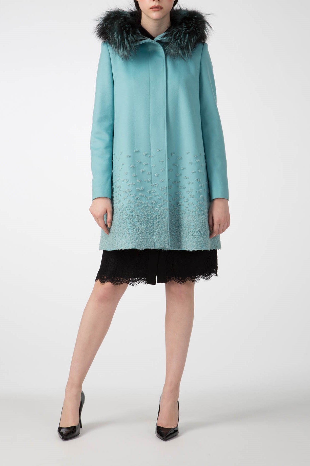 A person wearing the stylish Antonio Croce Carolina Textured Coat, complete with a detachable fur hood and decorative stitching, stands elegantly in black high heels over a black lace skirt against a plain white background.