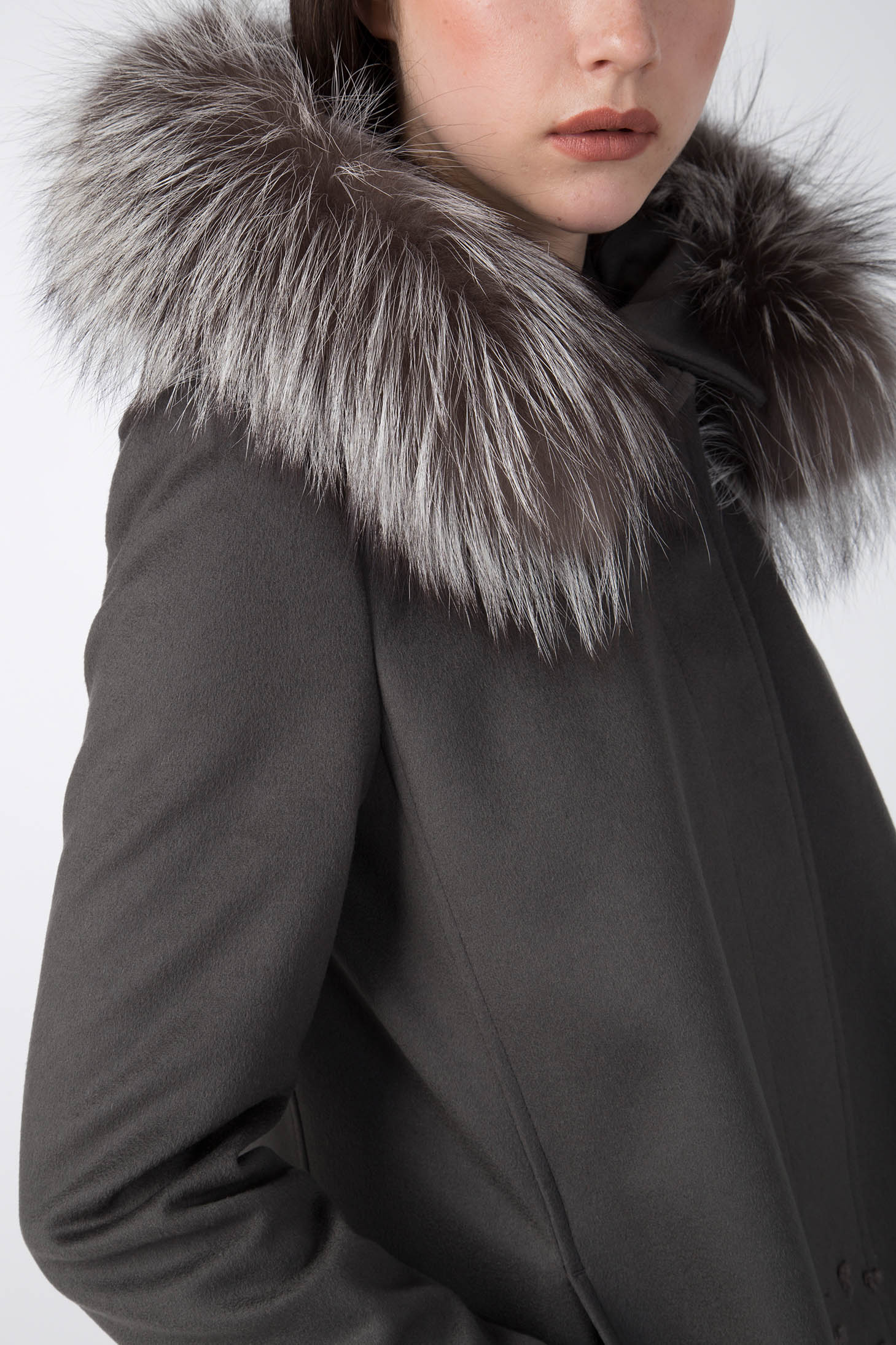 Close-up of an individual wearing the Antonio Croce Carolina Textured Coat with a dark winter design, featuring a detachable grey fur hood with white tips that adds a luxurious texture. The individual's face is partially visible, showcasing a neutral expression.