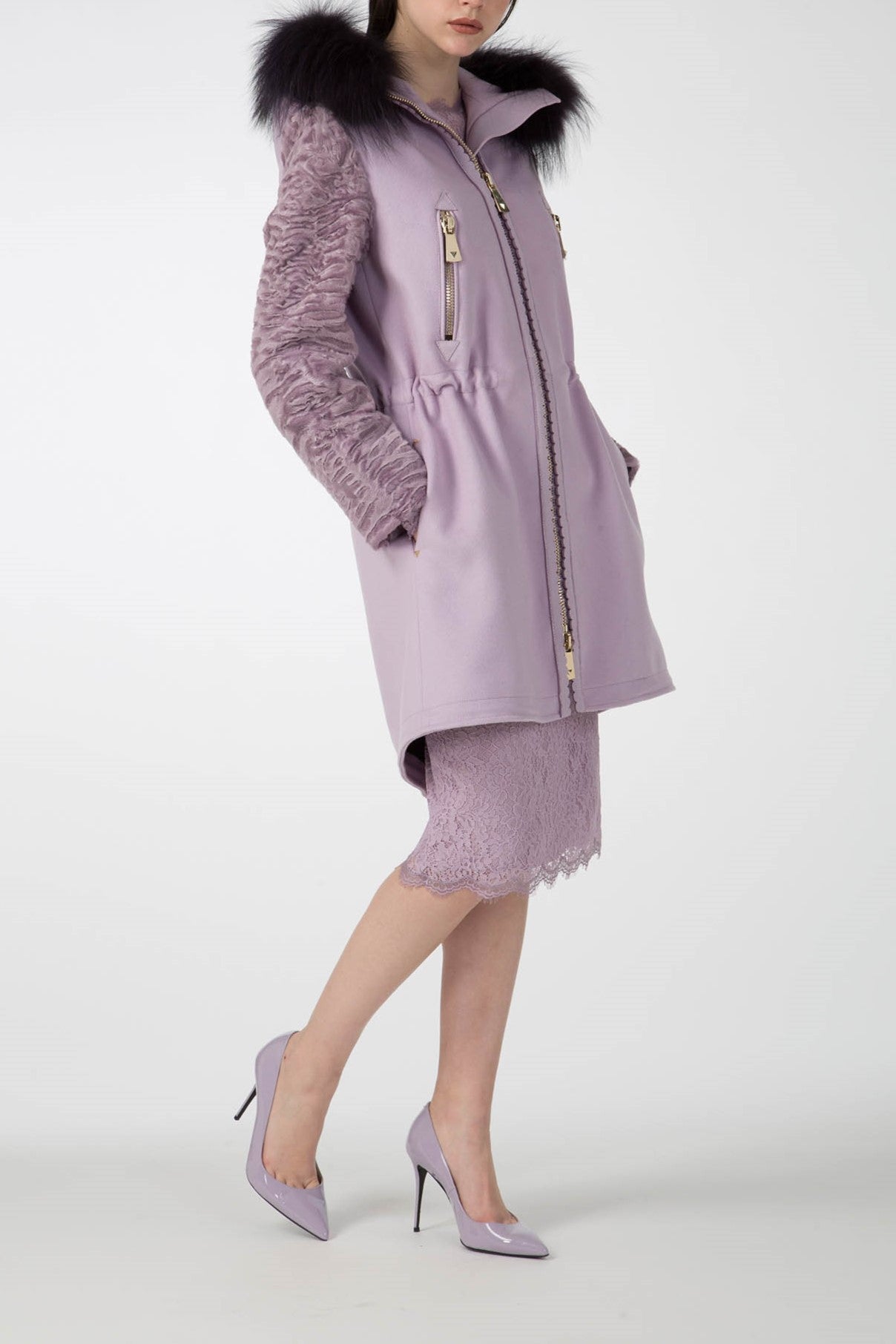 The individual is dressed in an Antonio Croce Catrina Coat accented with a luxurious fur trim and textured sleeves in a striking light purple. The ensemble includes a matching lace skirt and pointed high-heeled shoes, all set against a plain white background.