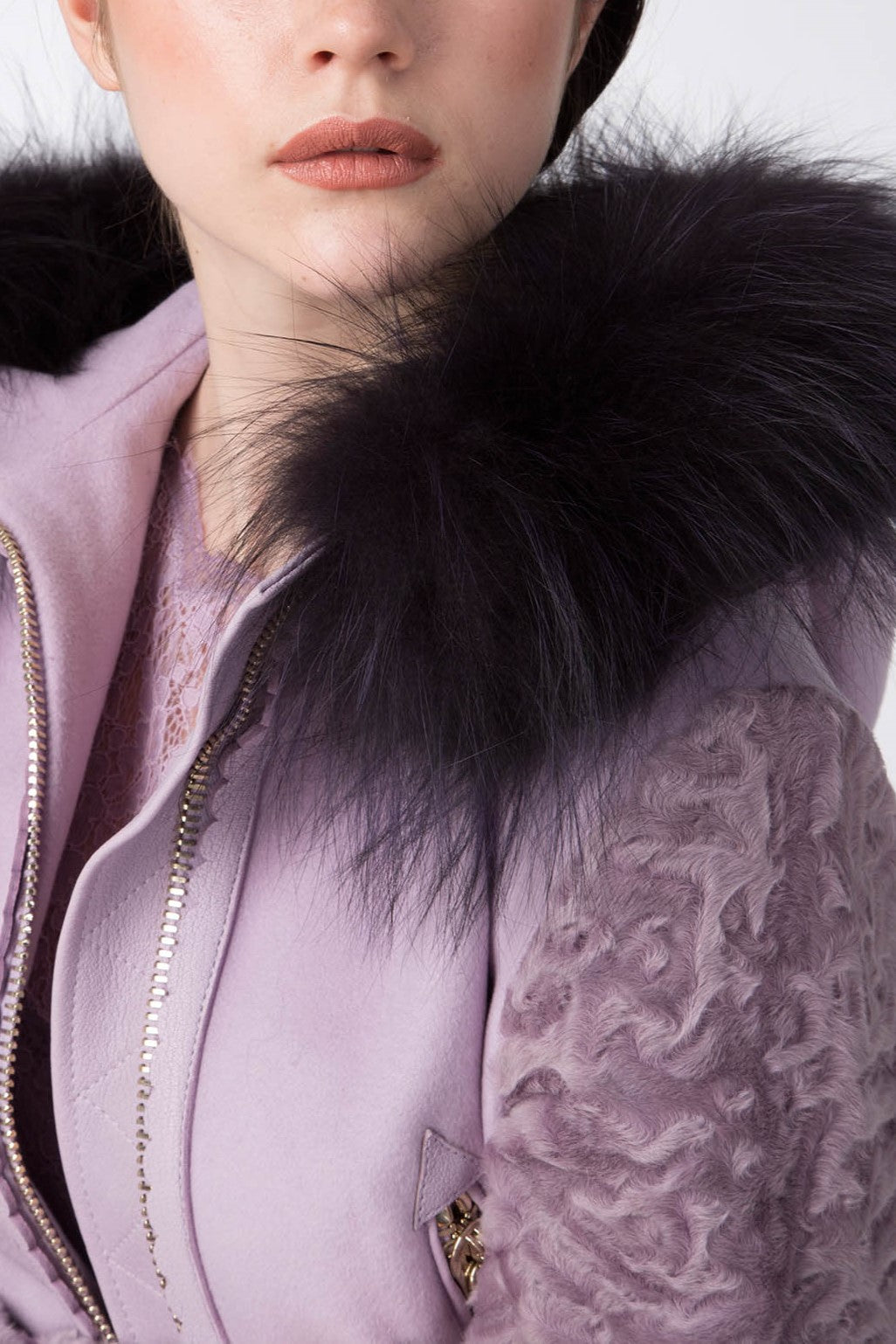 A person wearing the Antonio Croce Catrina Coat, a striking light purple design featuring a black faux fur collar and textured sleeves with a visible zipper. Their neutral makeup complements their light skin, although only the lower part of their face and body is visible.