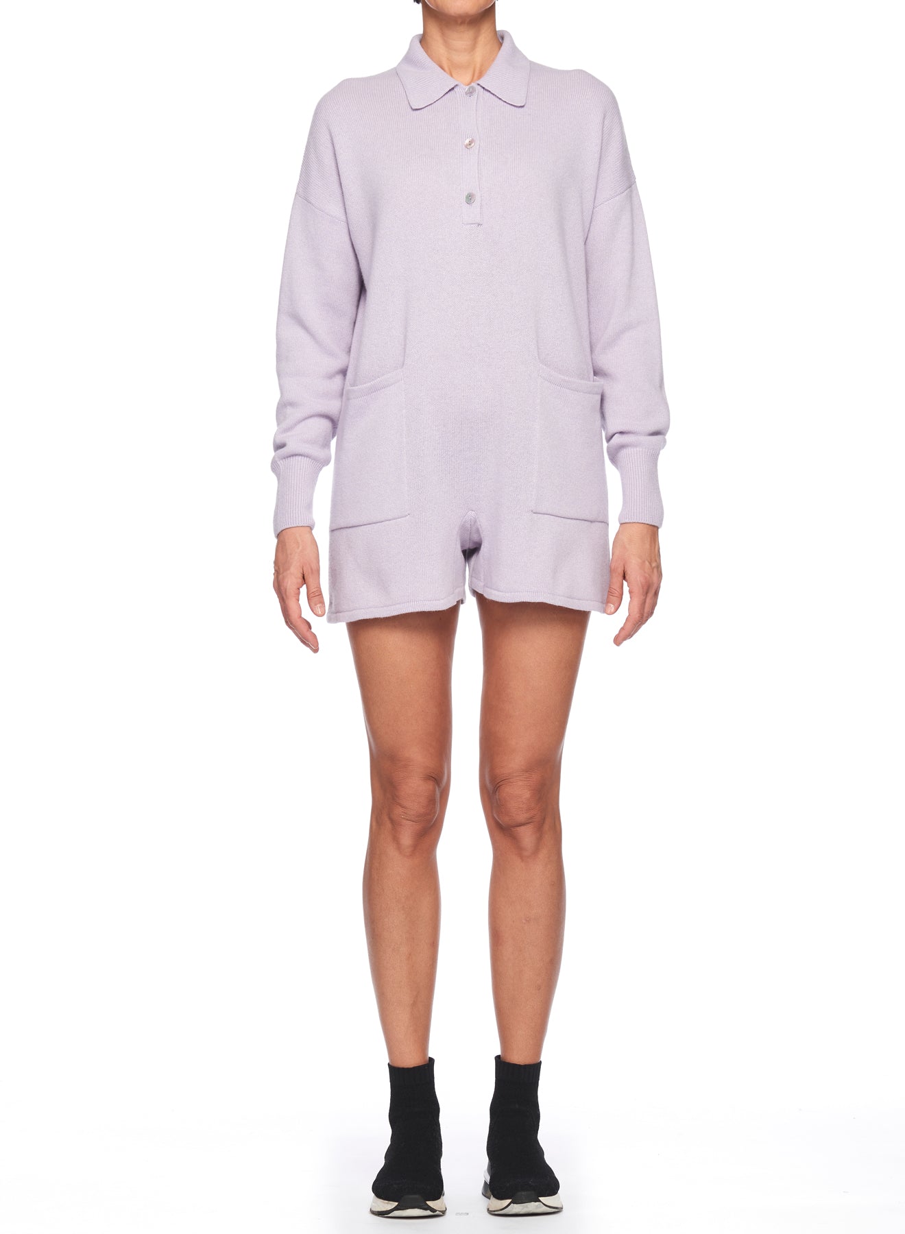 A person wearing a Fuzzi Woman beige polo-neck knit jumpsuit stands against a white background. They are also wearing black ankle socks and sneakers.