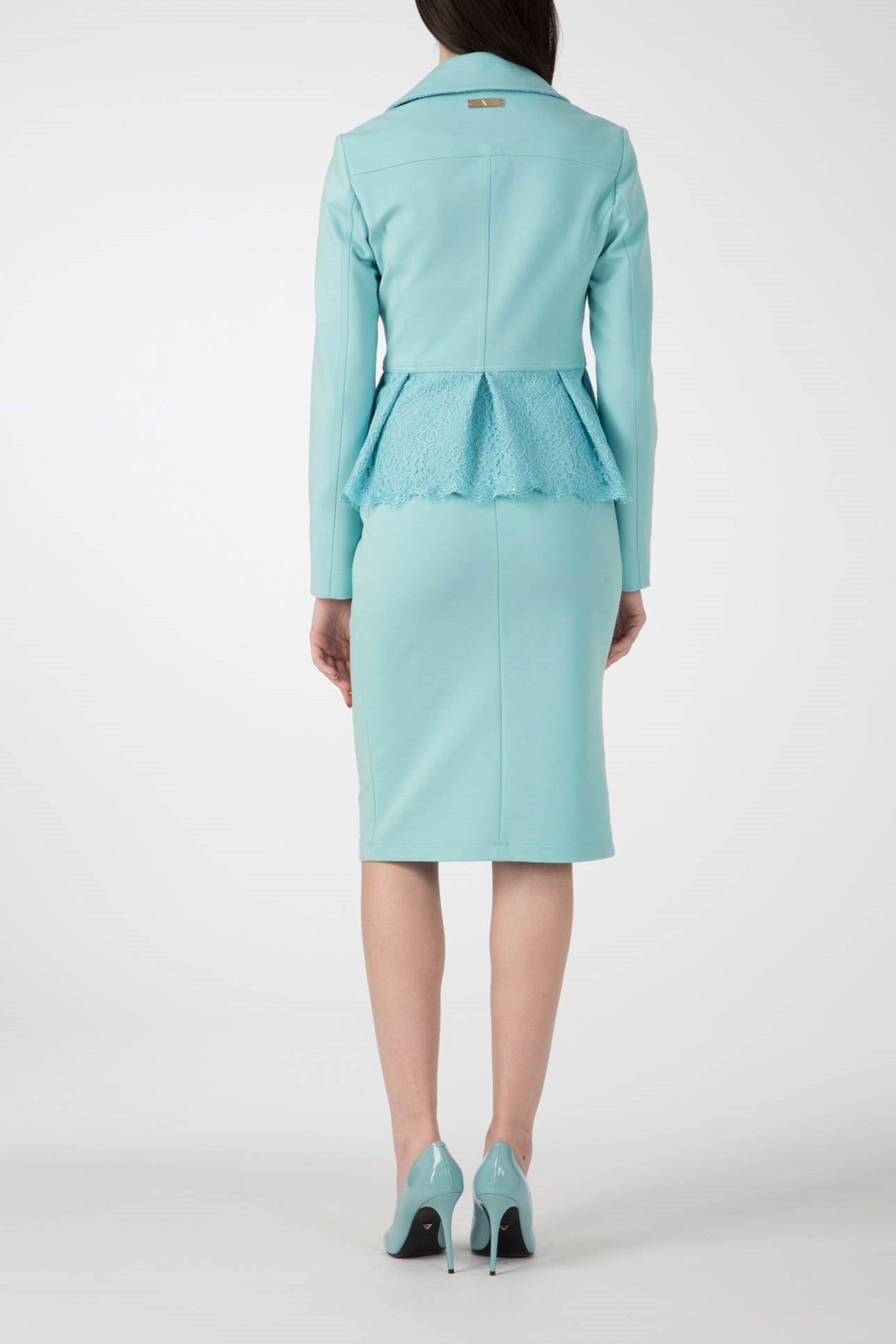 The back view shows a person dressed in the Antonio Croce Gigi Jacket with Gold Hardware, a stylish light blue jacket featuring an edgy peplum detail, paired with a matching pencil skirt. The look is finished with light blue high-heeled shoes boasting an asymmetric zipper and shiny gold accents. The backdrop is plain white.
