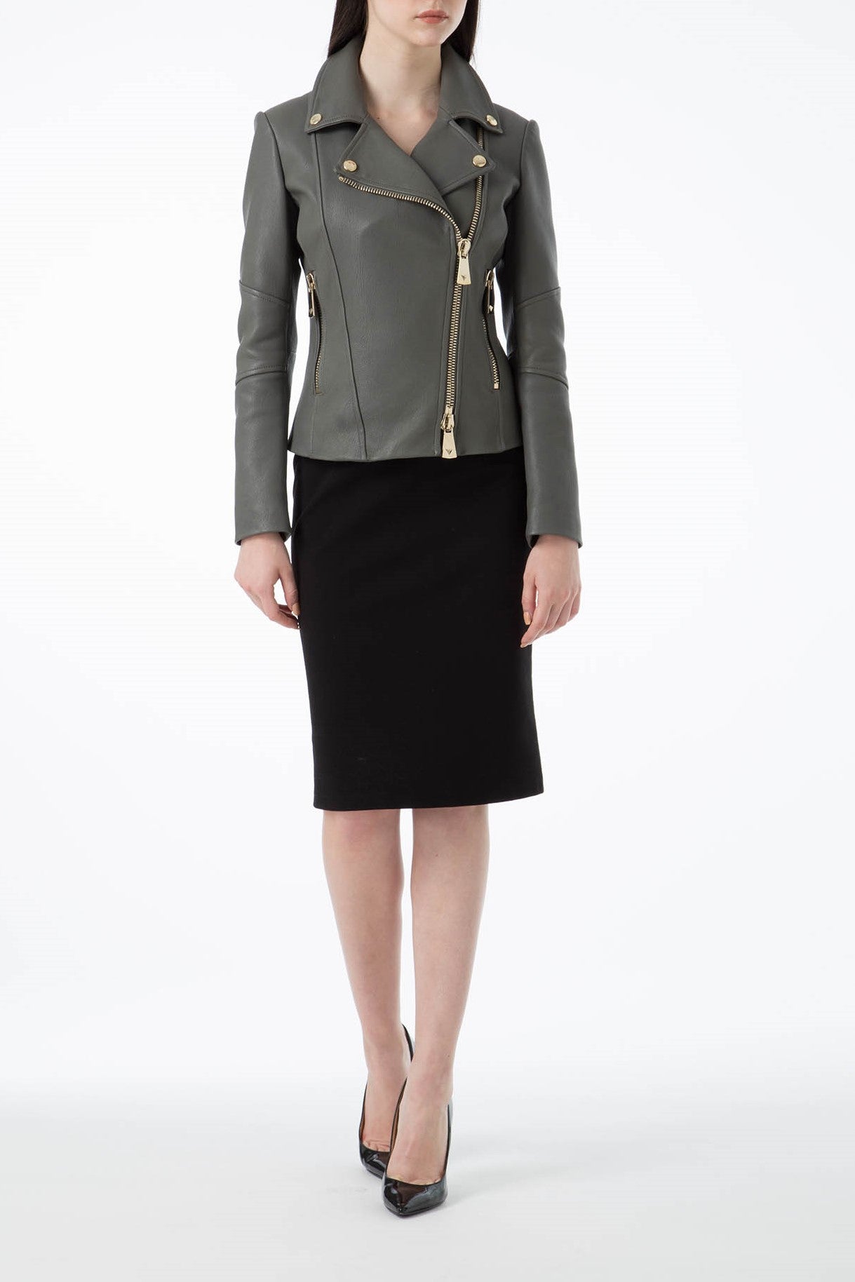 A person wearing the Antonio Croce Ginette gray leather jacket with gold hardware over a black knee-length skirt and sleek black high heels stands against a plain white background.