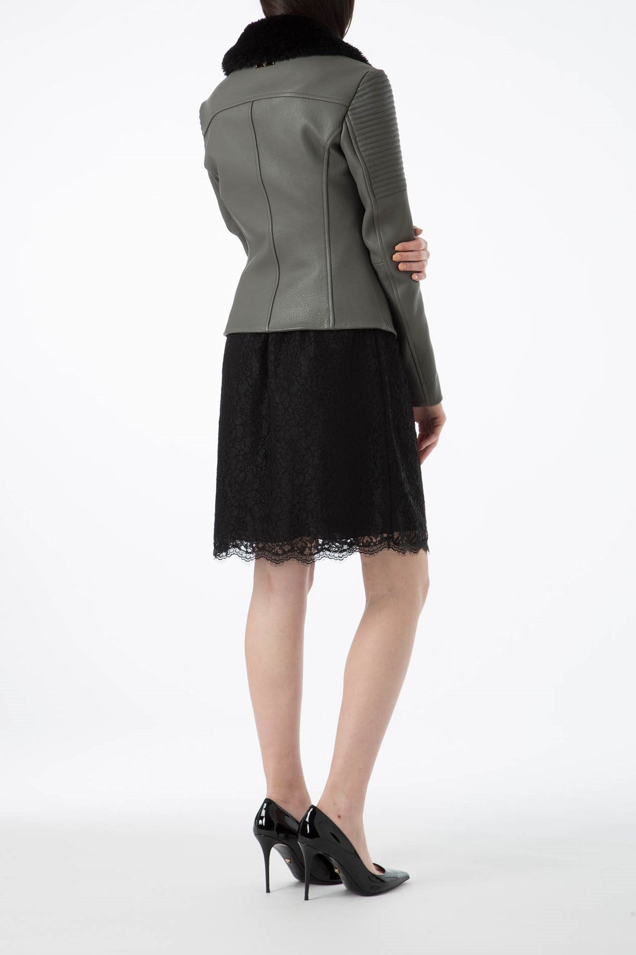 A person is seen from behind wearing the Antonio Croce Green Leather Jacket with a black fur collar. The jacket, featuring an asymmetric zipper closure, is stylishly paired with a black lace skirt and high-heeled shoes against a plain white background.