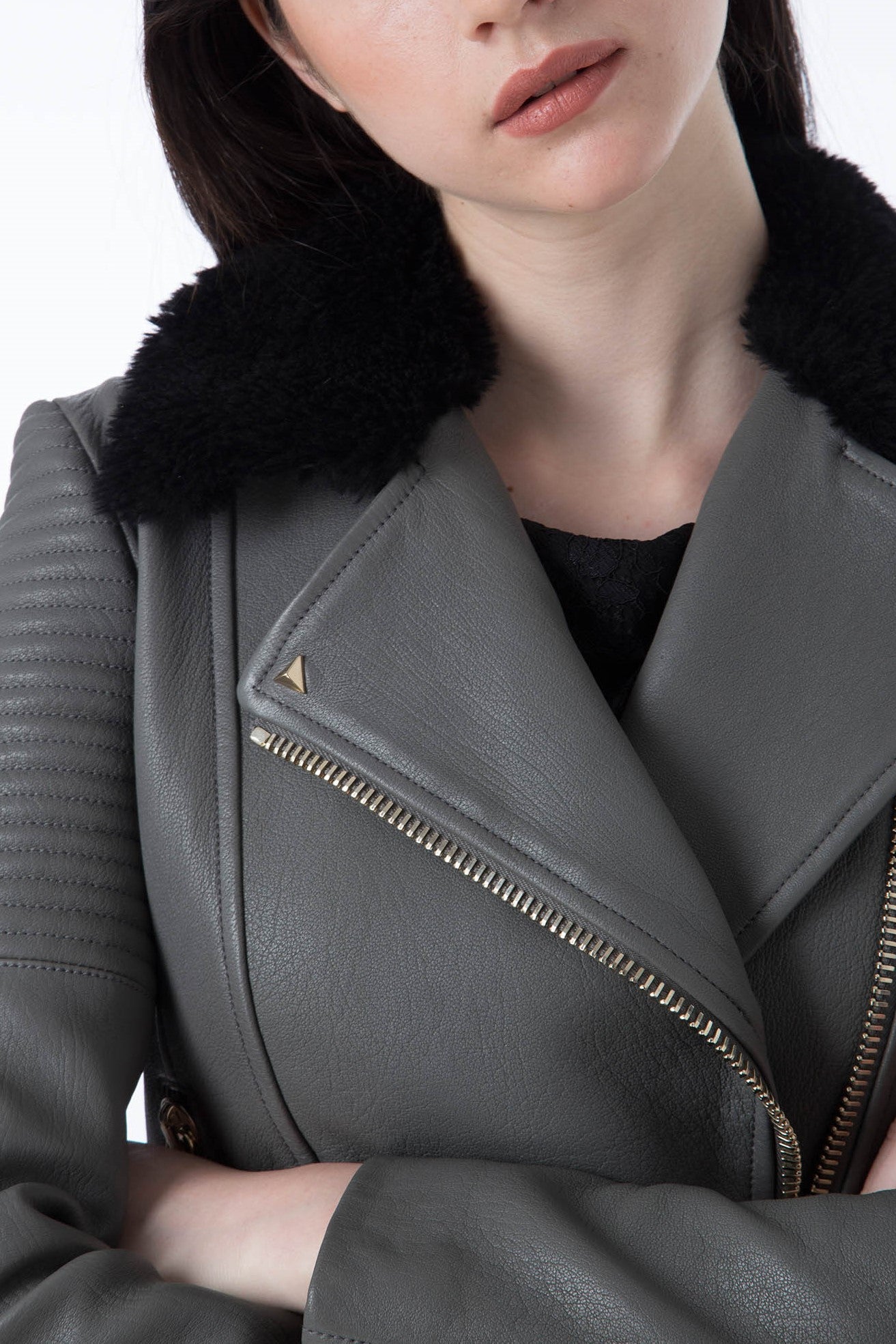 A person stands with arms crossed, wearing the Antonio Croce Green Leather Jacket featuring an asymmetric zipper closure that adds an edgy vibe. The black faux fur collar provides a luxurious touch, while quilted detailing on the sleeves completes the look against a plain white background.