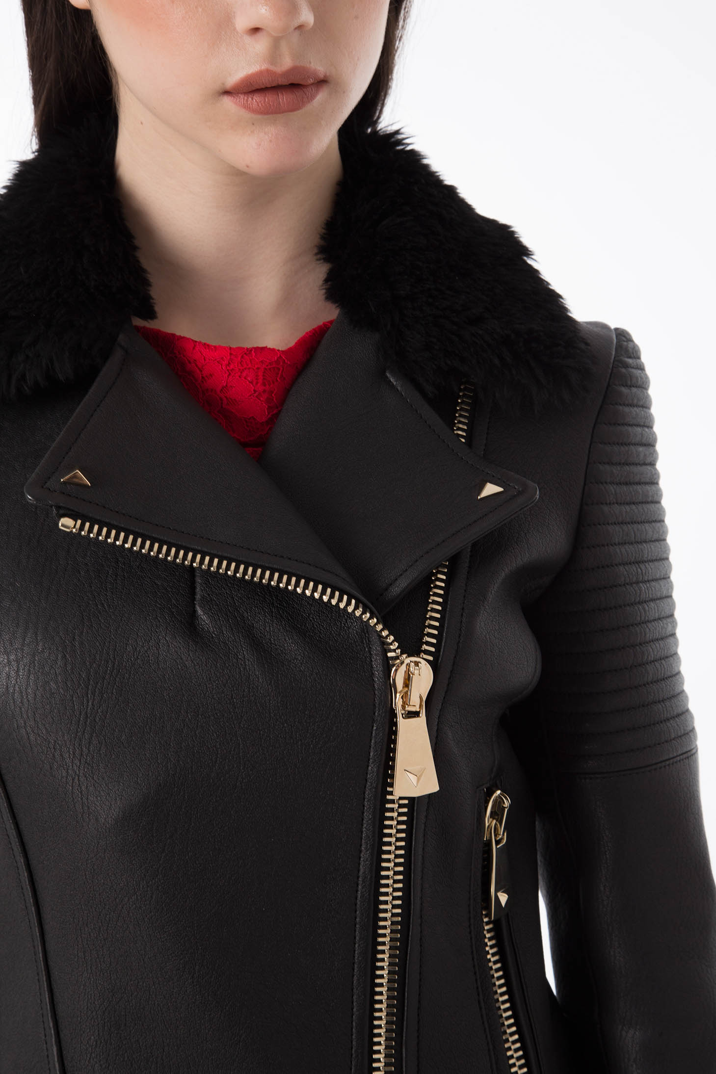 Close-up of a person wearing the Antonio Croce Green Leather Jacket with Fur Collar featuring edgy gold zippers and a luxurious fur collar. An asymmetric zipper closure adds flair, while underneath peeks a bold red garment. The plain white background highlights the partially visible face.