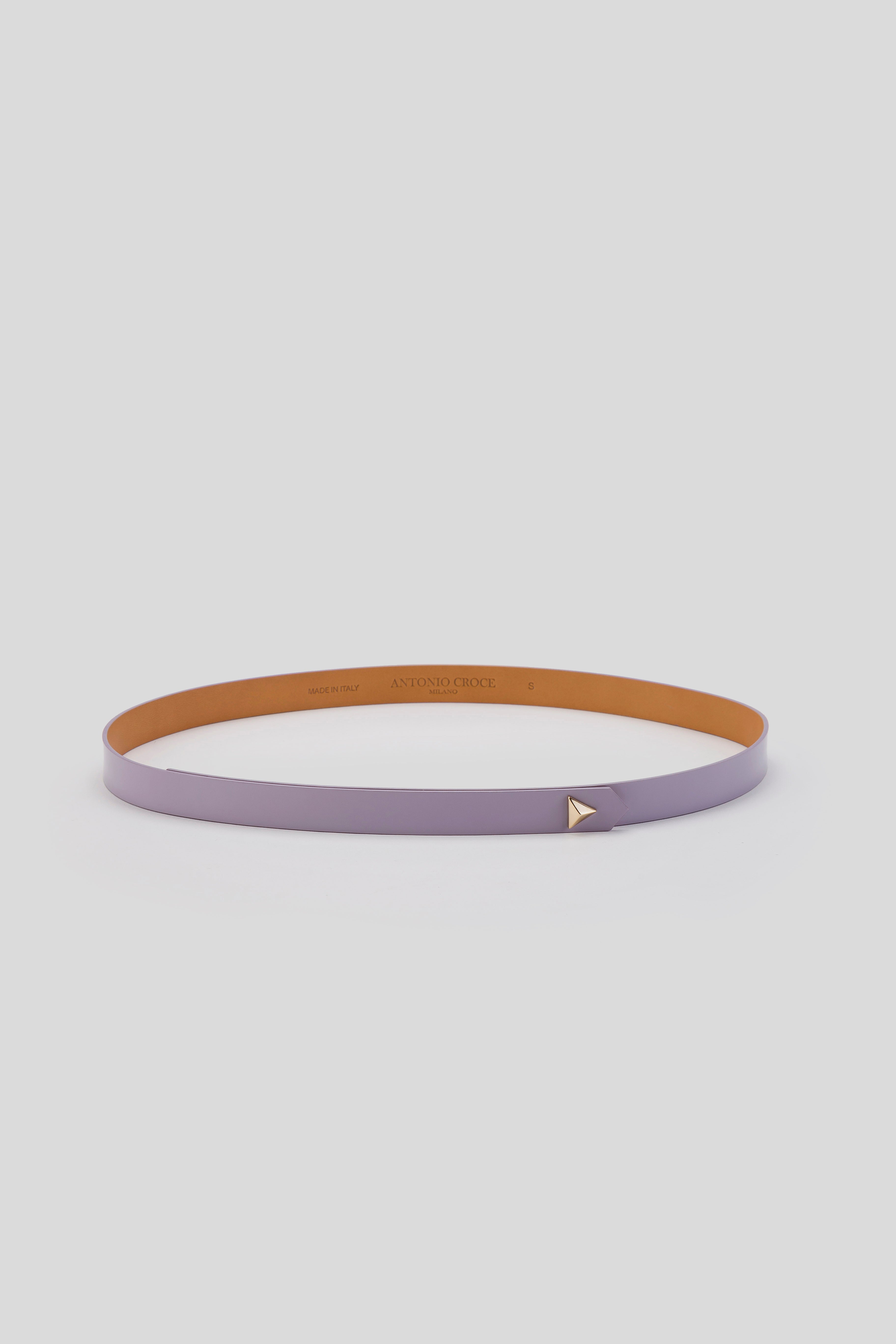 The Antonio Croce Lana Thin Belt by Antonio Croce displays a minimalist design in a soft lavender shade, complete with a small triangular gold buckle, set against a light gray background. Its sleek leather and understated elegance give it a vintage appeal, radiating timeless charm.