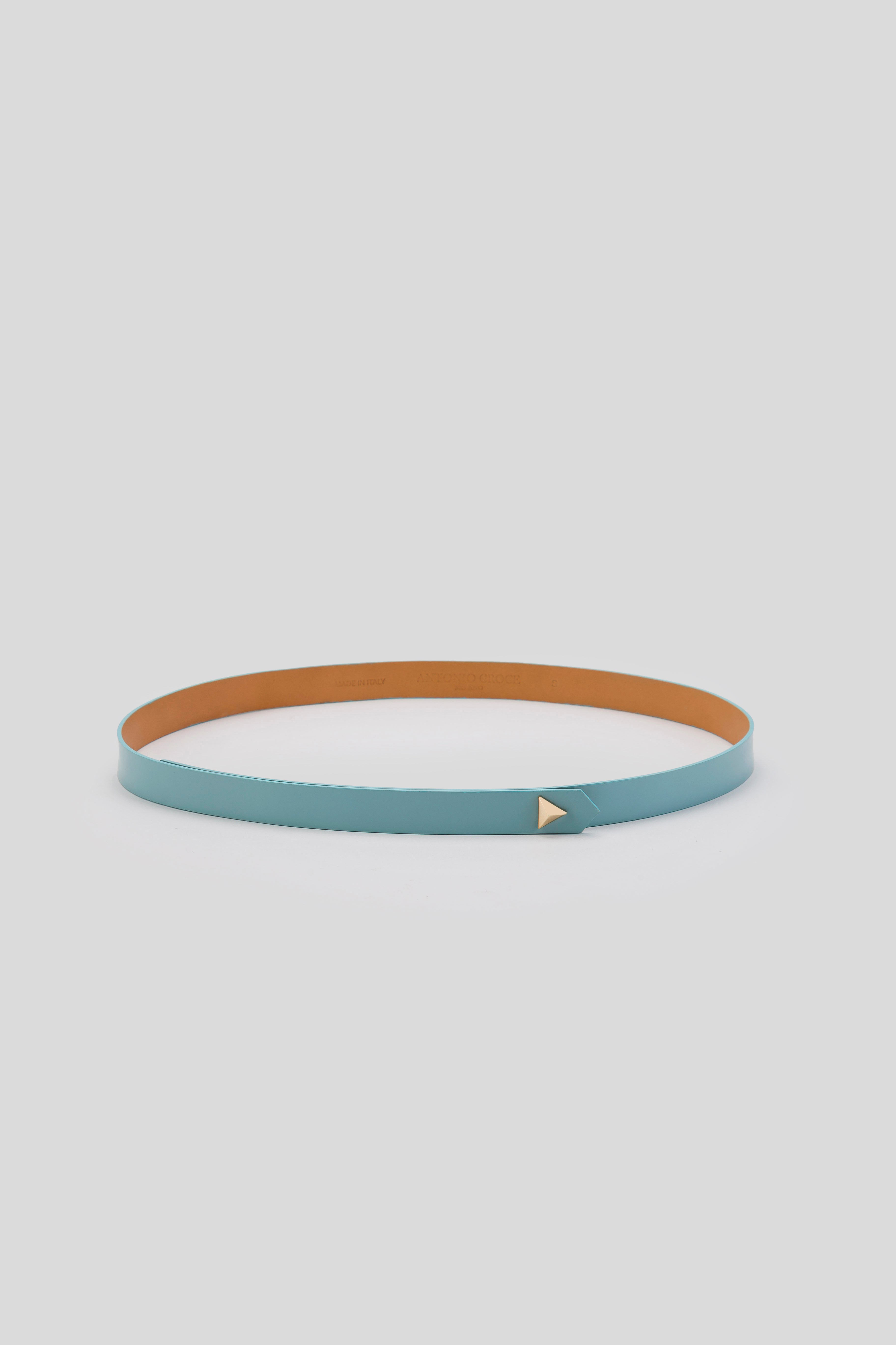 The Antonio Croce Lana Thin Belt, designed with a minimalist touch, is presented with a thin turquoise leather exterior and a tan inner lining. It features a small vintage-style gold triangle buckle and is arranged in a circular shape against a light gray background.