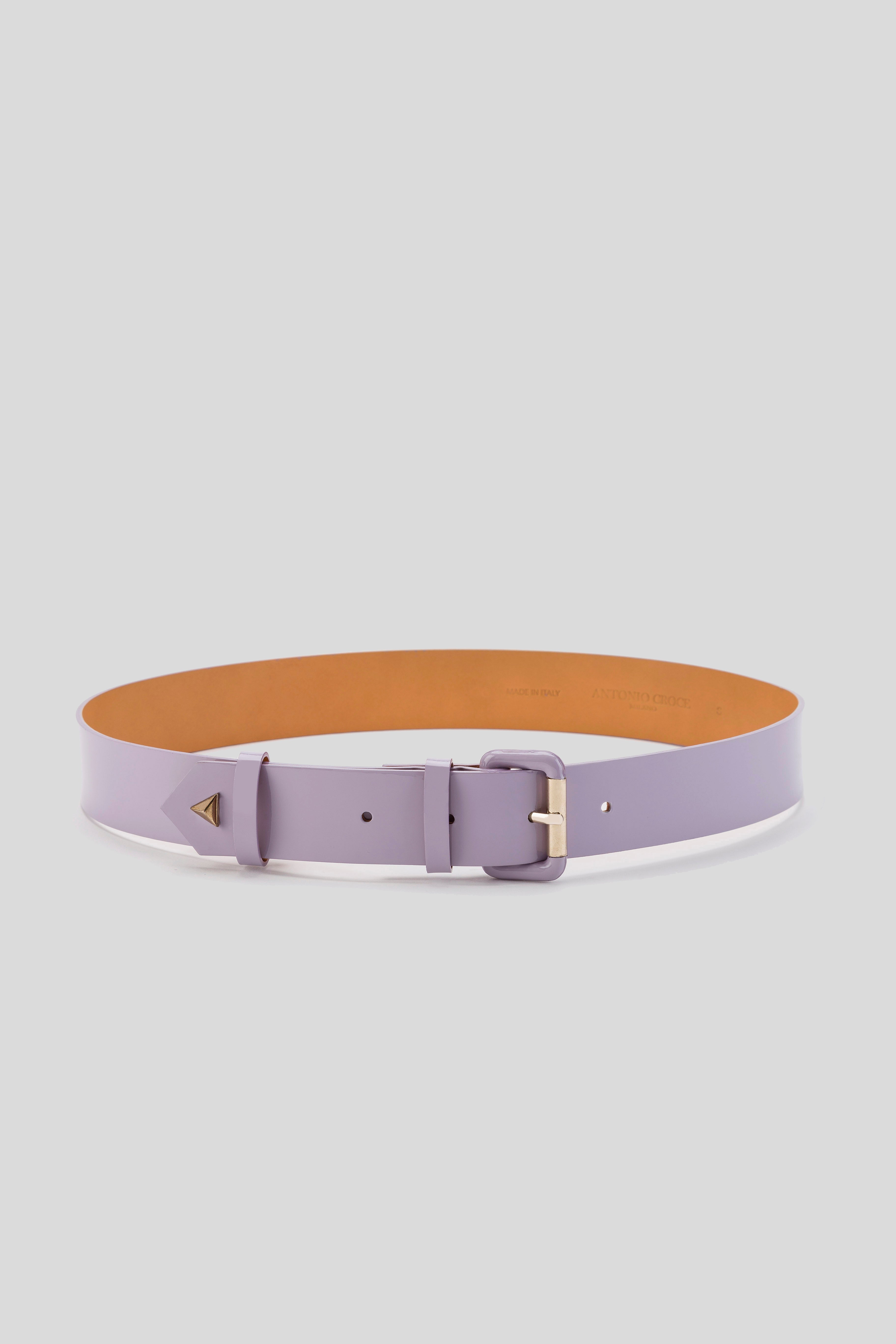 The Antonio Croce Lory Leather Belt with Gold Accents is displayed flat, highlighting its elegant minimalist design. The belt features a smooth light purple leather texture and a small triangular metal detail near the gold buckle, adding to its vintage charm. The interior of the belt is tan-colored.