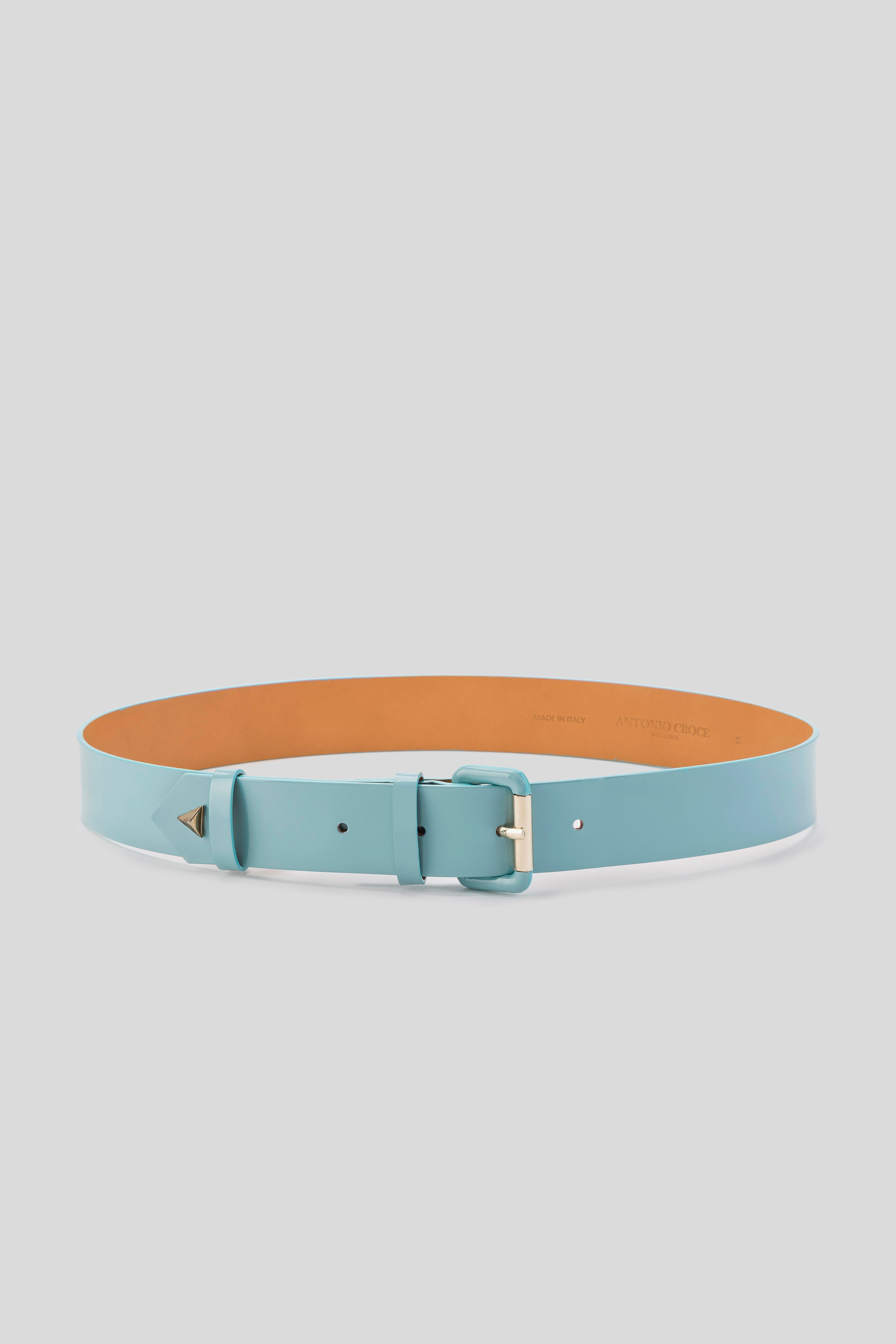 A light blue leather belt from Antonio Croce, named the Lory Leather Belt with Gold Accents, is displayed against a plain background. The belt features a smooth texture and tan interior, embodying minimalist design details reminiscent of a vintage piece.