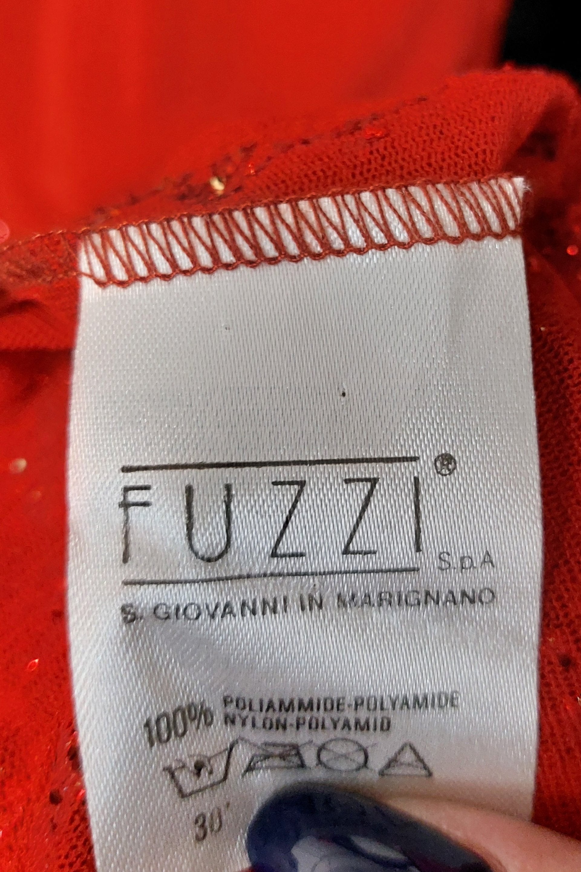 A clothing label held by a hand with dark blue nail polish reads Jean Paul Gaultier. This vintage piece, a red, glitter-covered dress from the Spring/Summer 1995 collection, is made of 100% polyamide and comes with washing instructions. It exudes glam reminiscent of the iconic Jean Paul Gaultier era.