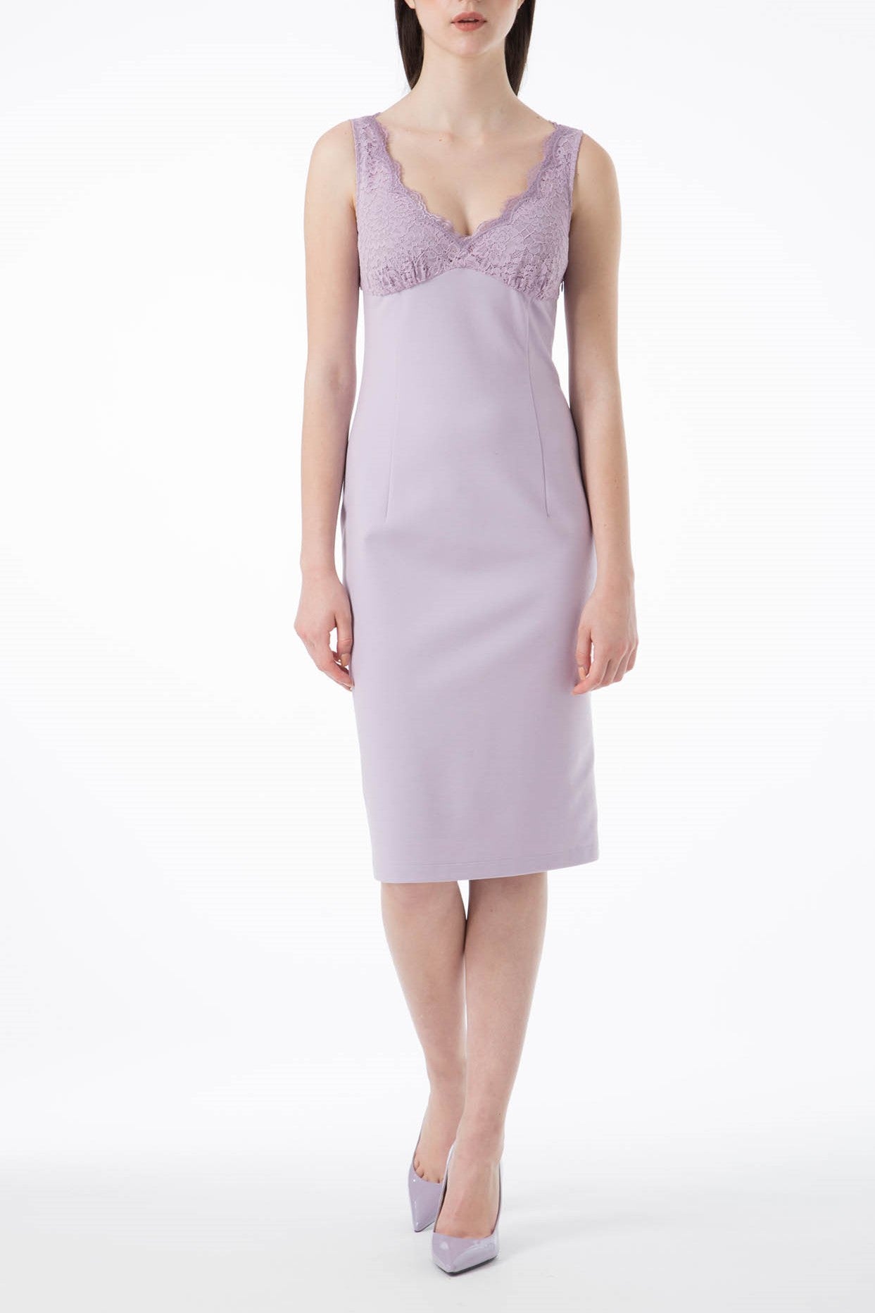 A woman in the exquisite Antonio Croce Alanna Evening Dress, featuring an elegant lavender sleeveless design crafted from luxurious stretch fabric with lace detailing on the bodice, stands against a white background. She completes her stylish look with matching lavender high heels.