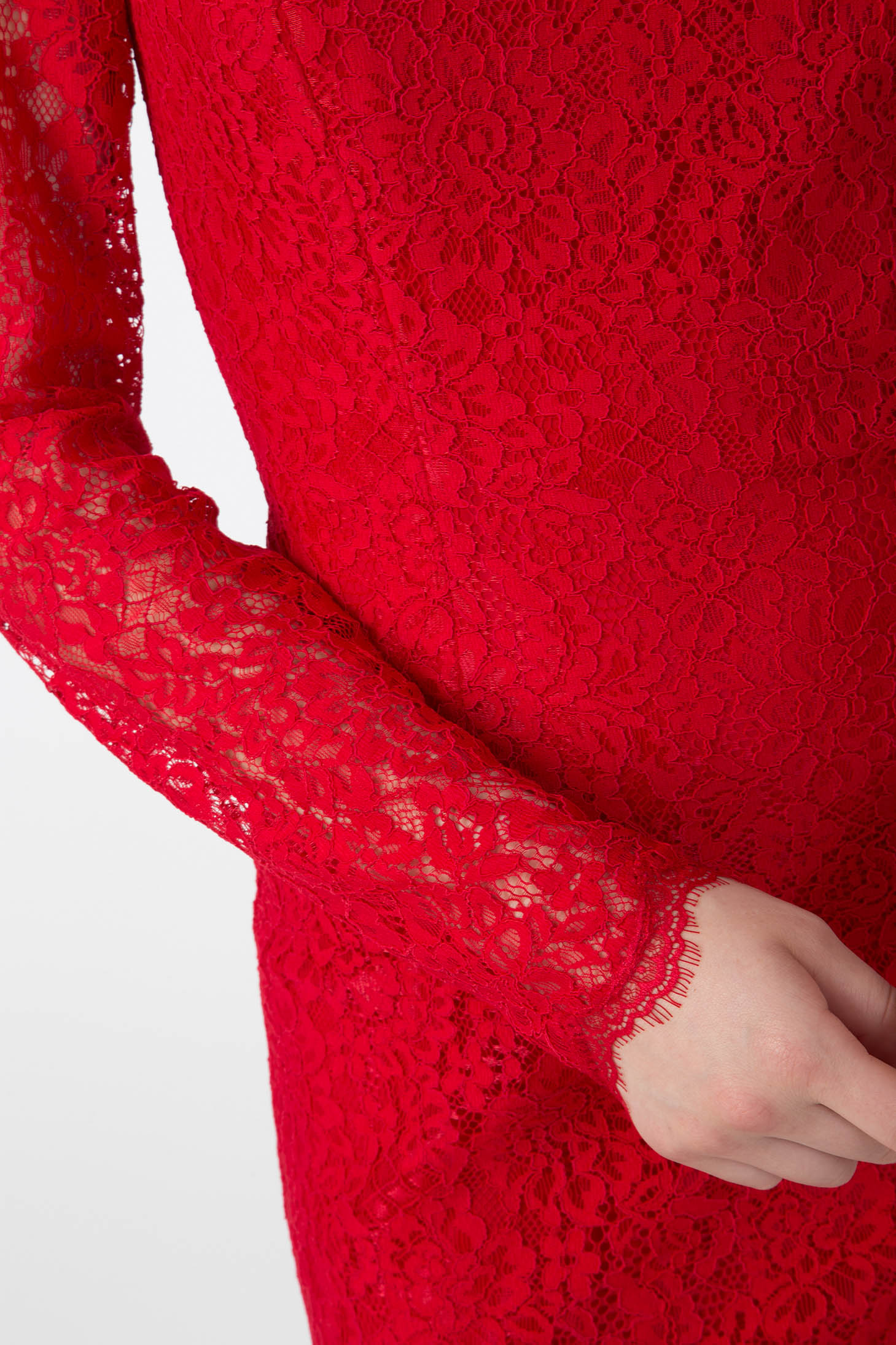 Close-up of a person in the striking Antonio Croce Ambeta Long-Sleeve Lace Dress, exuding an elegant look. The dress features intricate floral patterns in vibrant red lace. One arm is bent, with a hand gently resting near the side.