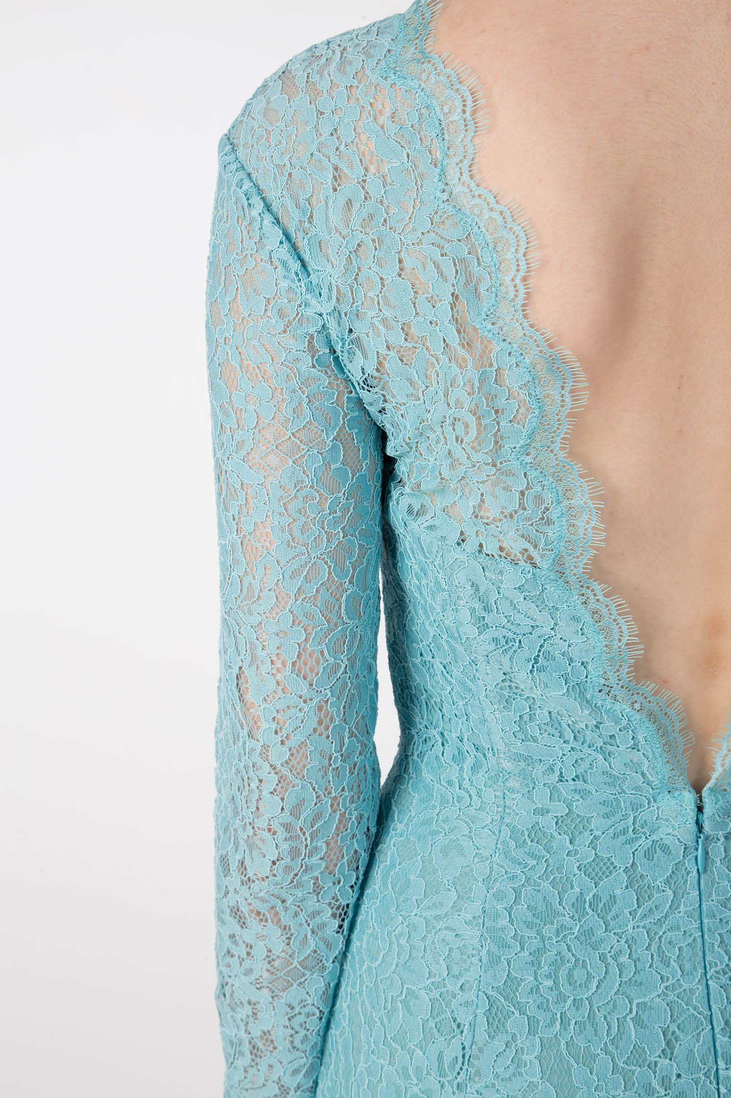 A close-up shot captures someone wearing an Antonio Croce Ambeta Long-Sleeve Lace Dress. This vintage piece features a striking turquoise color with a deep V-back. The intricate lace pattern enhances its elegant look, highlighting the delicate design against a plain white background.