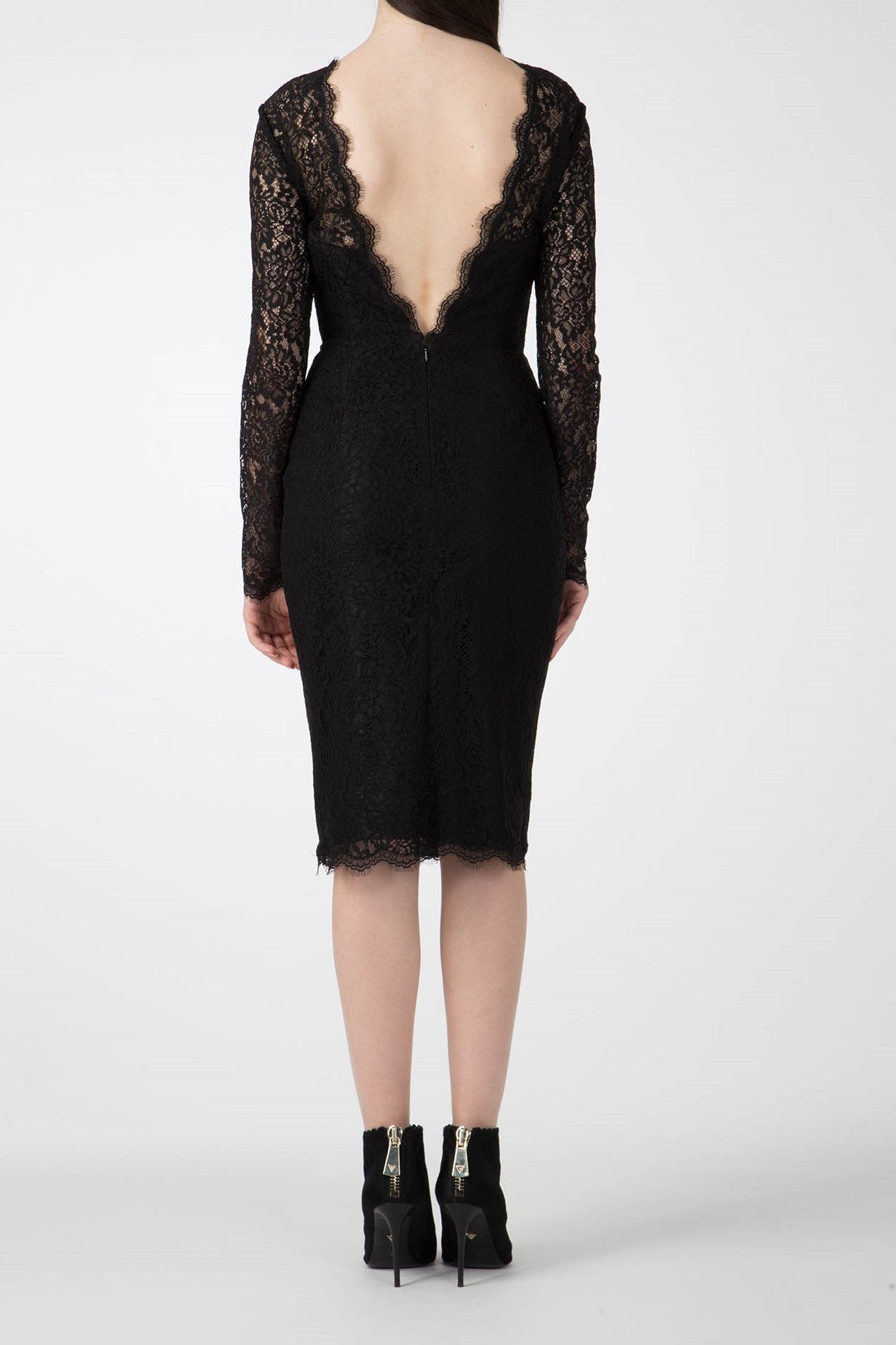 A woman in the elegant Antonio Croce Ambeta Long-Sleeve Lace Dress, featuring a deep V-back, stands facing away. This vintage piece is paired with her ankle-high black boots adorned with zippers. The background is plain white.