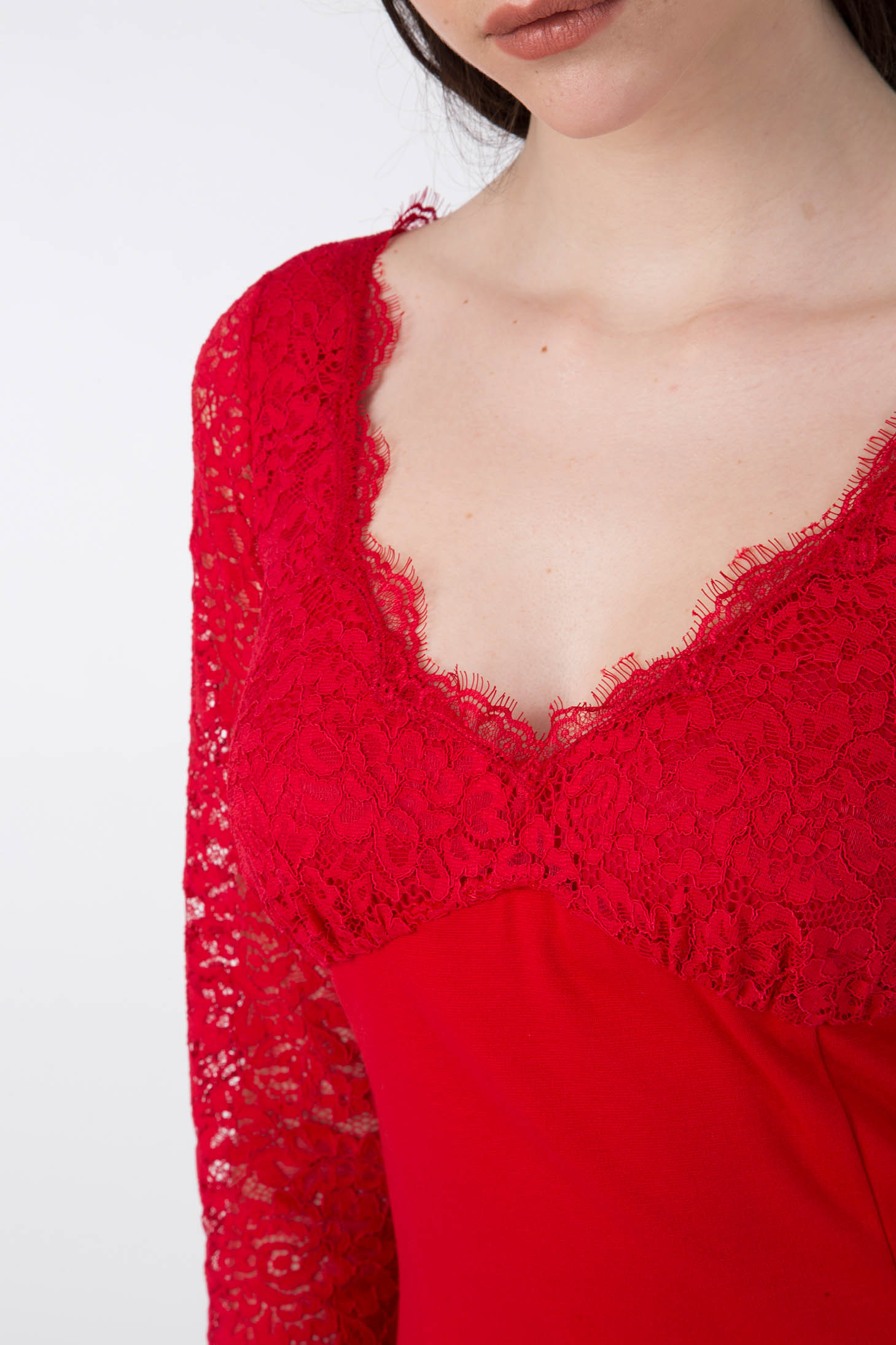 A woman showcases the Antonio Croce Ampara Embroidered Lace Dress, featuring intricate embroidery and vibrant red hues. The delicate lace fabric embellishes the sleeves and V-neckline, perfectly complementing her long dark hair cascading over her shoulders against a simple, light background.