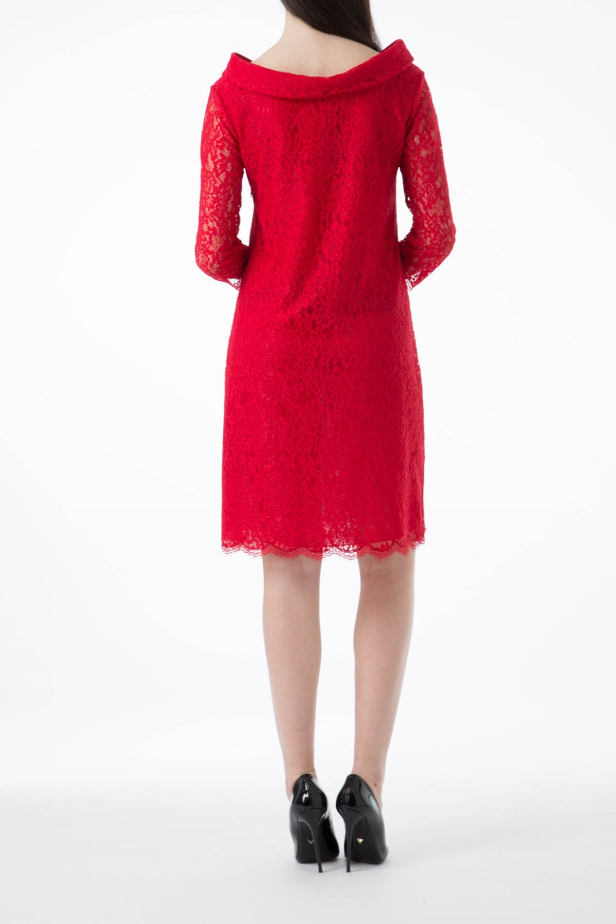 A woman stands facing away, exuding a vintage vibe in the Antonio Croce Ana Romantic Lace Dress, which is knee-length with long sleeves and colored red lace. She pairs it with black high heels against a white background.