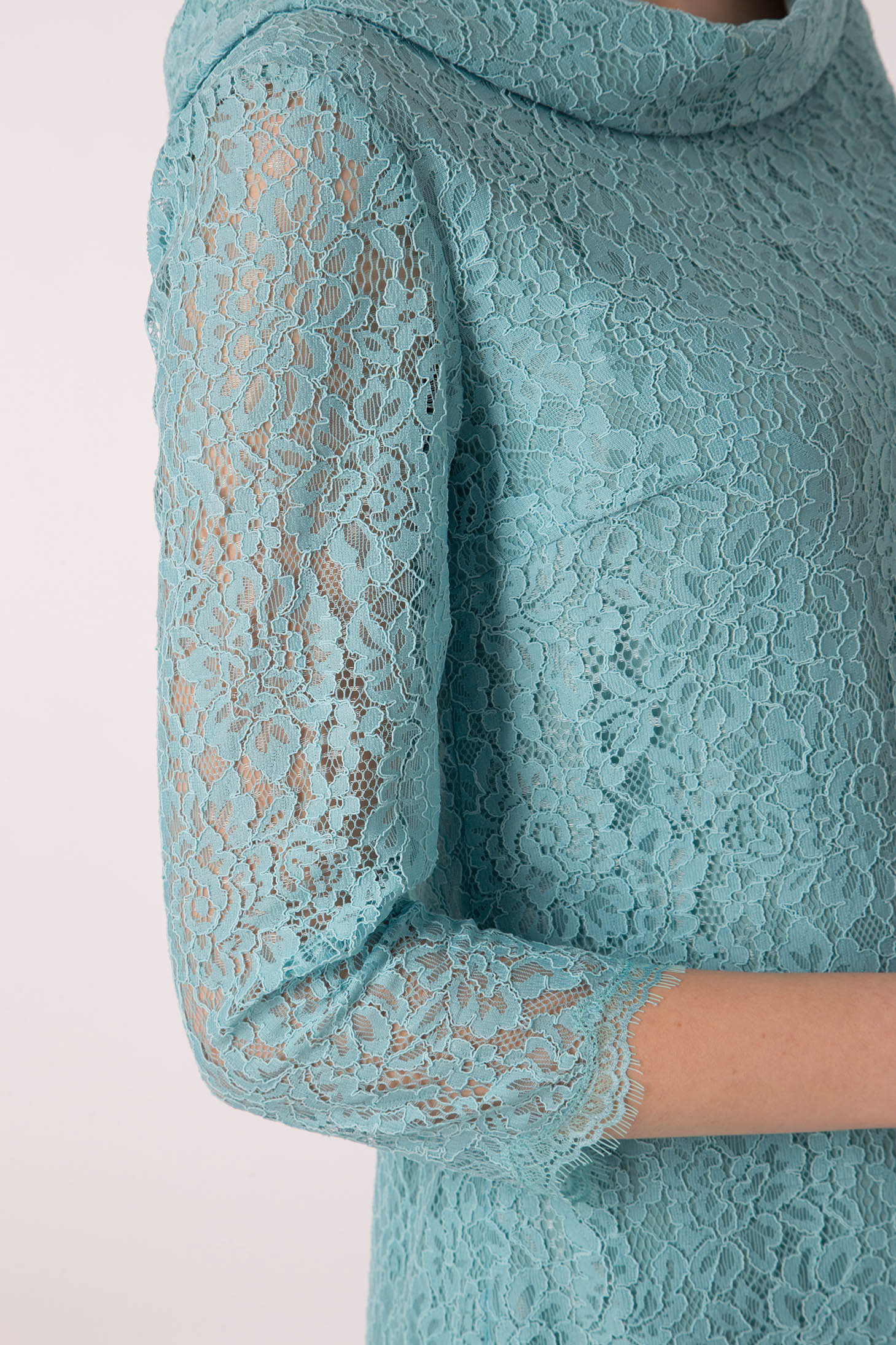 A close-up of a person wearing the Antonio Croce Ana Romantic Lace Dress, featuring a turquoise vintage lace design with three-quarter sleeves. The dress displays an intricate floral lace pattern against a plain white background, enhancing its elegant texture.