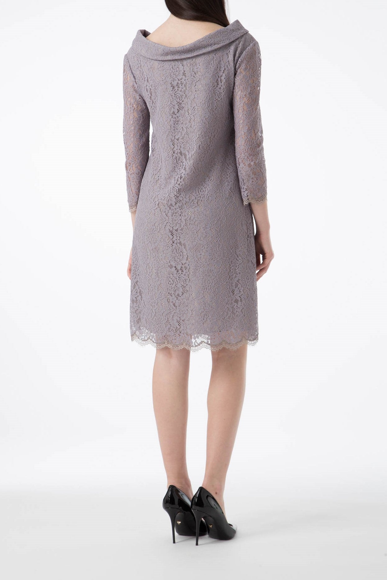 A woman stands with her back to the camera, highlighting the Antonio Croce Ana Romantic Lace Dress in a vintage light purple hue, featuring three-quarter sleeves and a scalloped hem. Her outfit is elegantly completed with chic black high-heeled shoes against a plain white background.