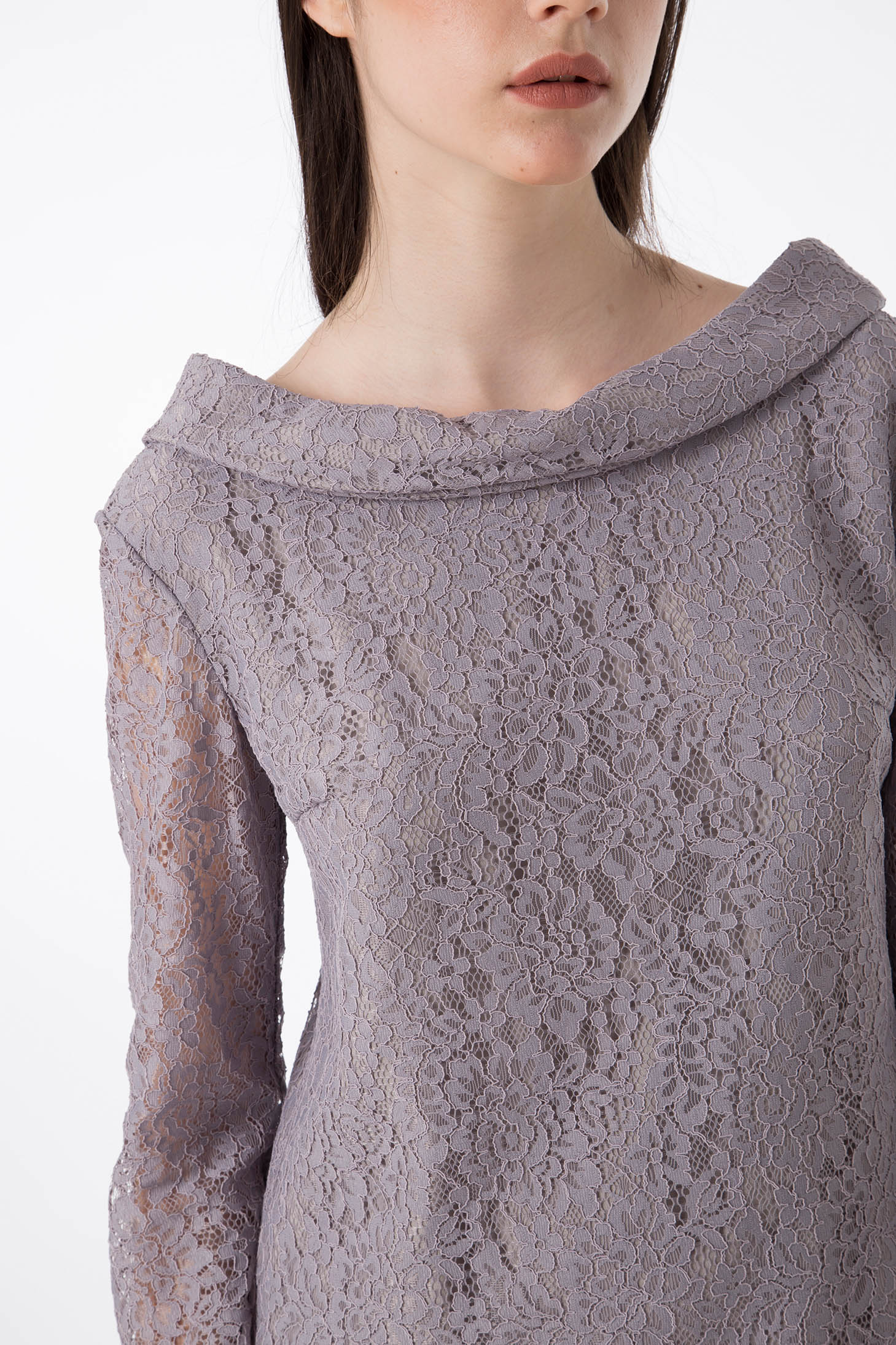 A person wearing the Antonio Croce Ana Romantic Lace Dress, characterized by its exquisite light purple vintage lace design, long sleeves, and wide, folded neckline. The photo features the upper body and part of the face, drawing attention to the intricate lace pattern. A plain white background accentuates the timeless elegance of this Antonio Croce creation.