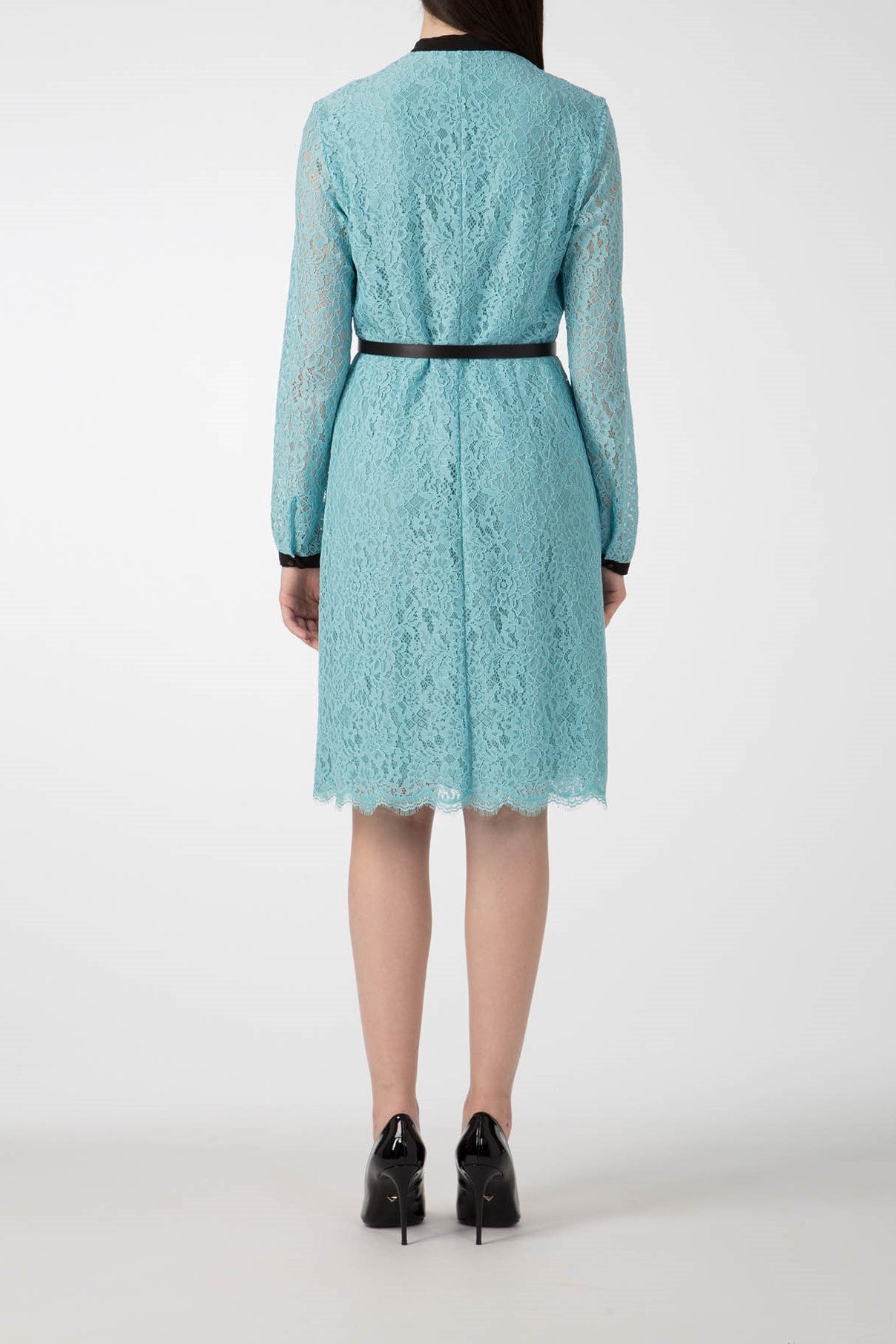 Rear view of a person wearing the Antonio Croce Anis Lace Shirt Dress with Bow in light blue. This knee-length, long-sleeved dress from Antonio Croce features a slim black belt, a scalloped hem, and is paired with black high-heeled shoes against a plain white background.