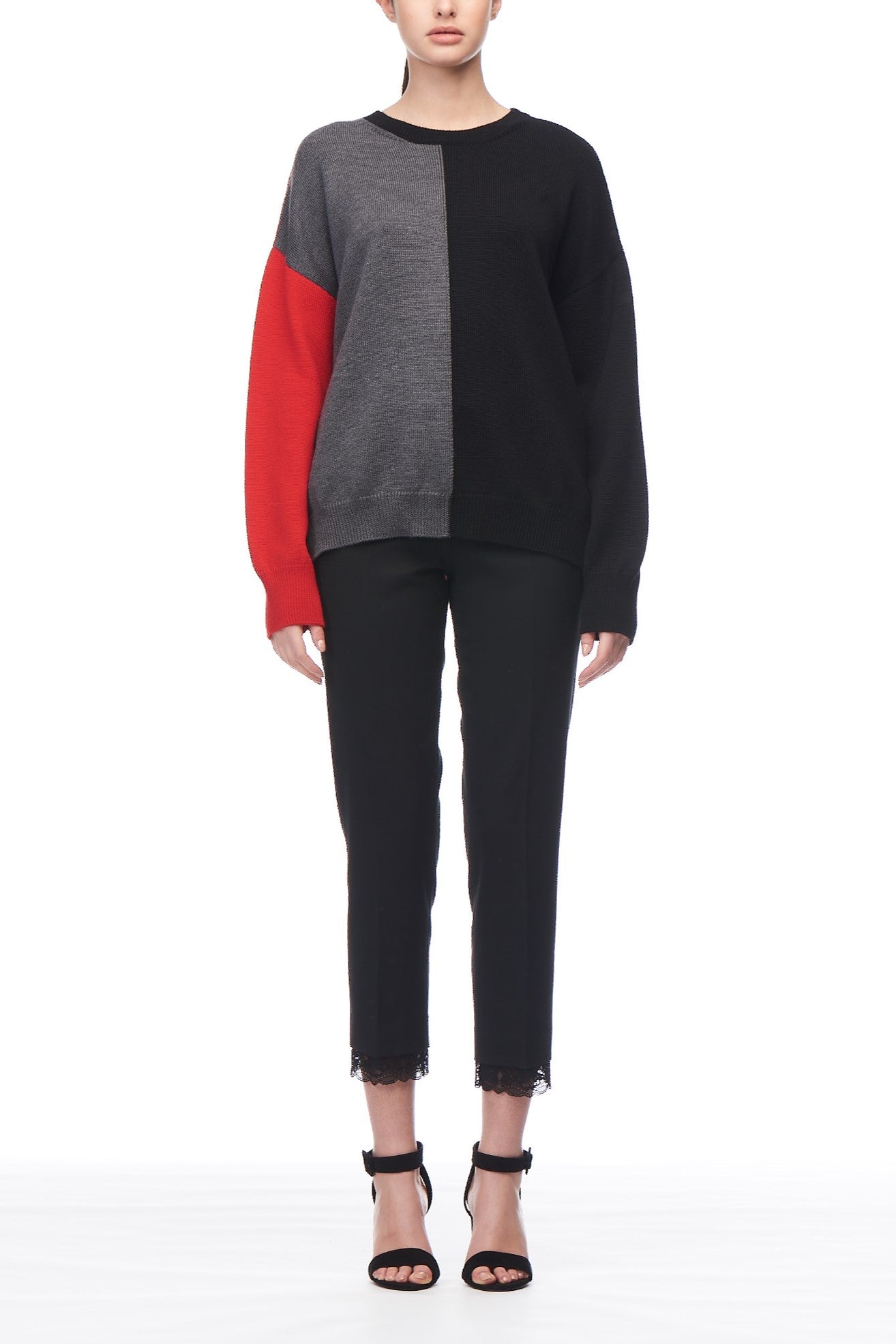 Dressed in an elegant Fuzzi Woman Round Neck Sweater showcasing vintage color-blocking in gray, black, and red, the person pairs this with chic black ankle-length pants enhanced by lace trim and fashionable black high-heeled sandals, all set against a plain white background.