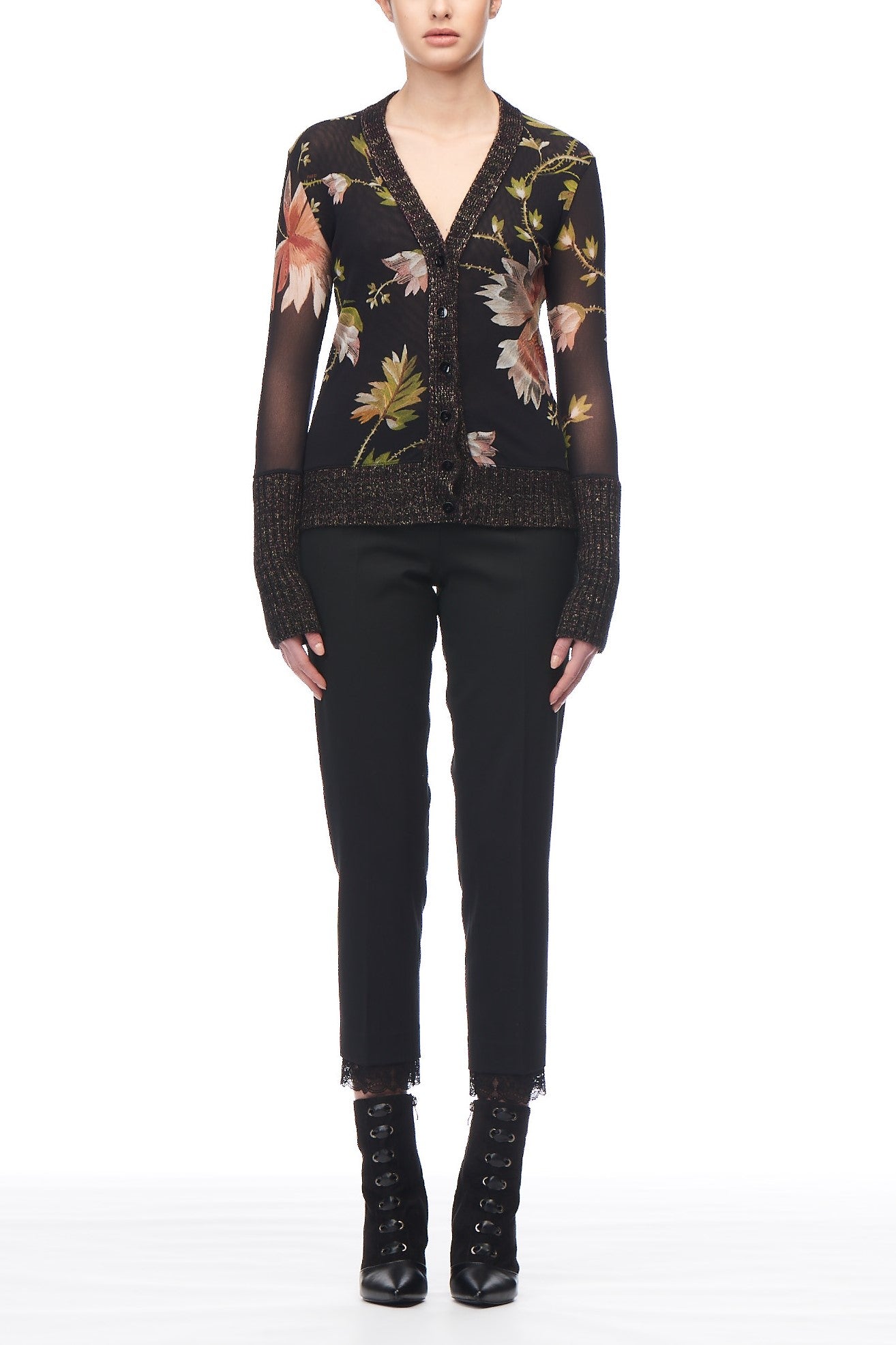 A person wearing the Fuzzi Woman Floral Cardigan—a vintage piece with large, colorful floral patterns and sheer sleeves—paired with black pants and lace-up boots, stands against a white background. The individual’s face is not visible.