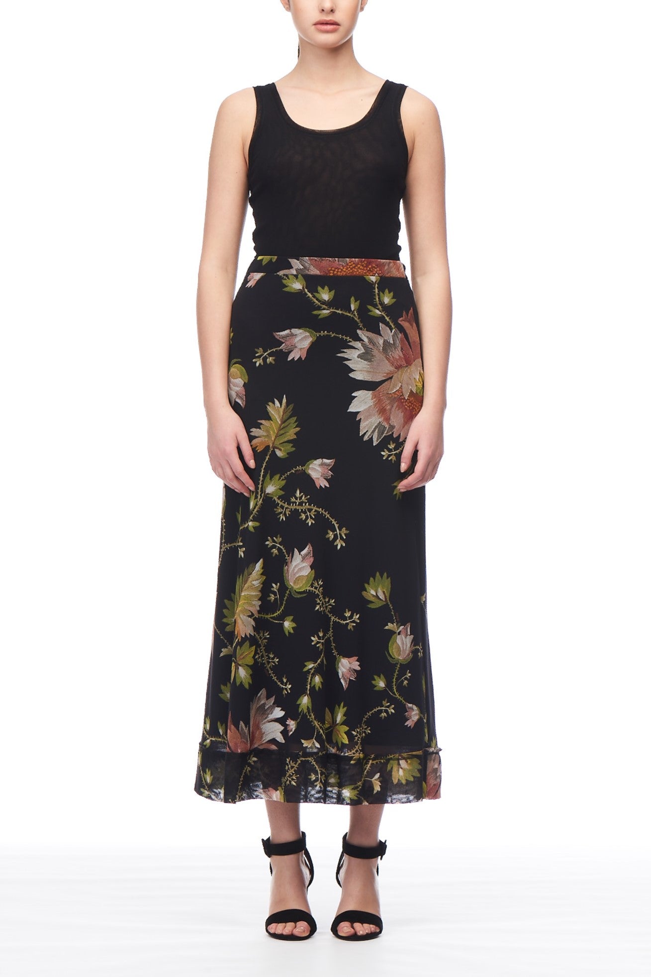 A person wearing a sleeveless black top and the Fuzzi Woman Floral Maxi Skirt by Fuzzi, standing against a plain white background while sporting black strappy heels.