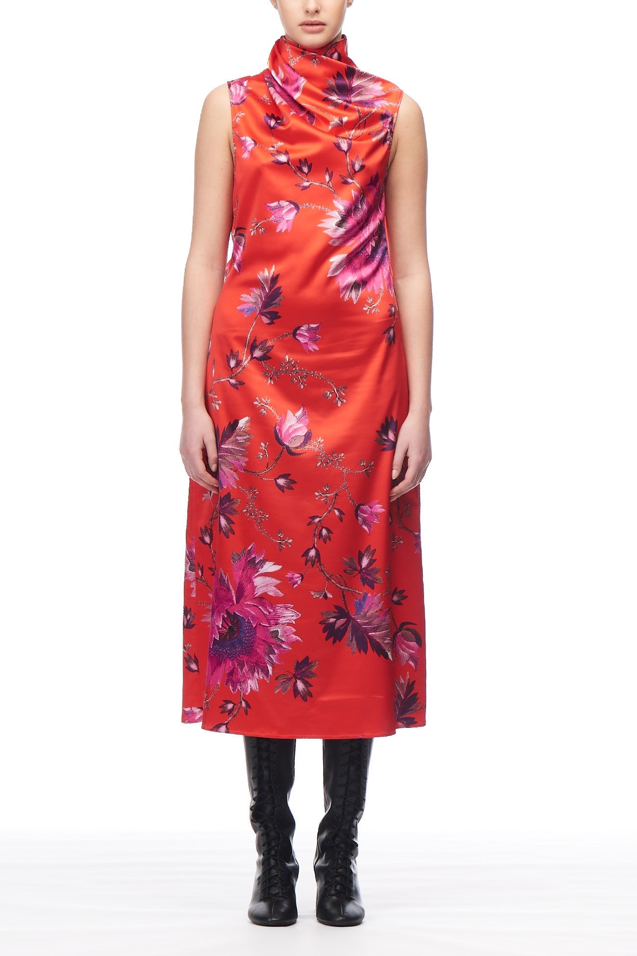 A person wearing the Fuzzi Woman Floral Long Dress in a vibrant orange sleeveless, high-neck style with a striking floral print stands against a white background. They are also wearing black lace-up boots.