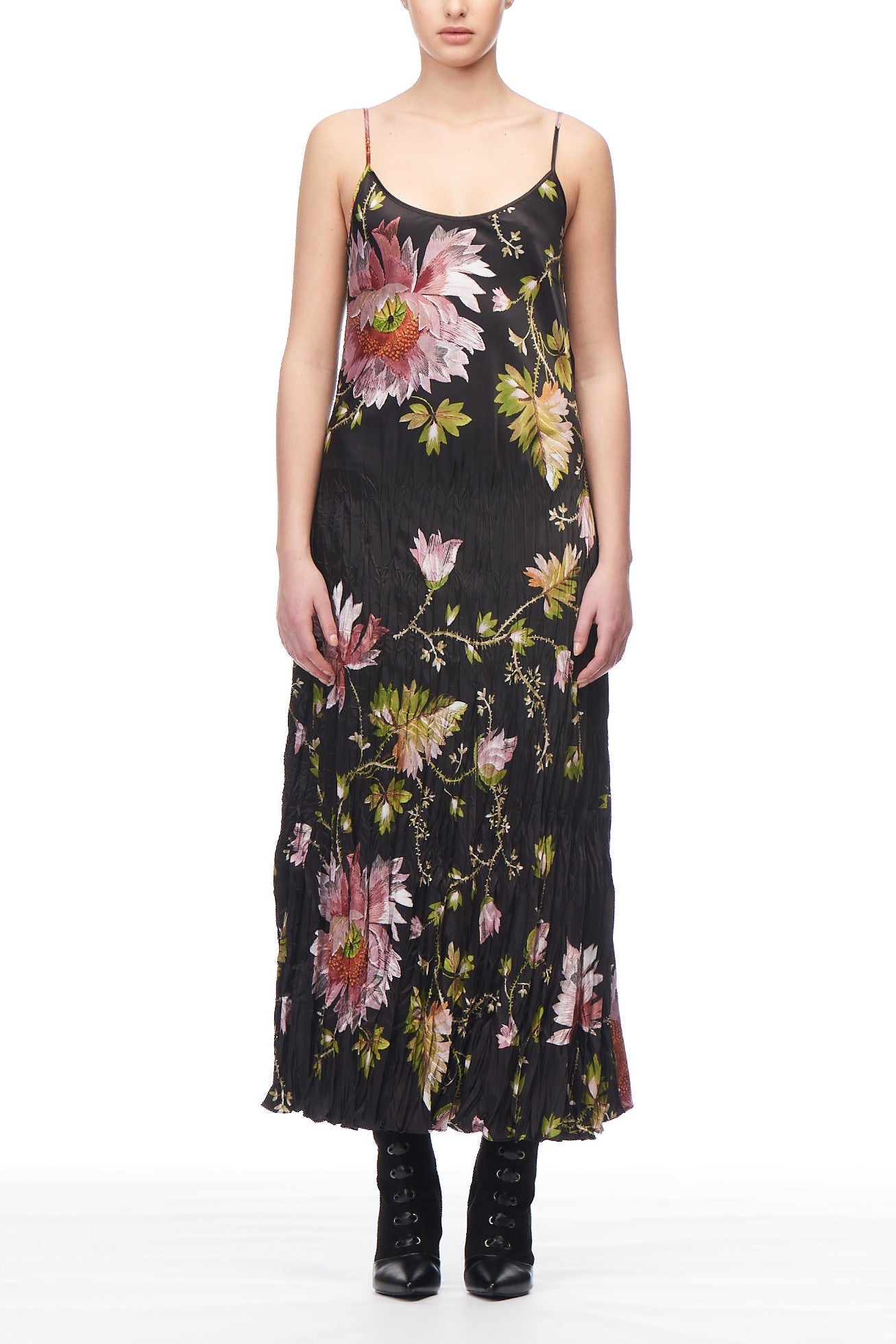 The individual is showcasing a Fuzzi Woman Floral Maxi Dress by Fuzzi, which is a long black dress with spaghetti straps and ruching, beautifully embellished with large pink and green floral embroidery. They have elegantly paired it with black silk ankle boots adorned with laces, all set against a pristine white background.