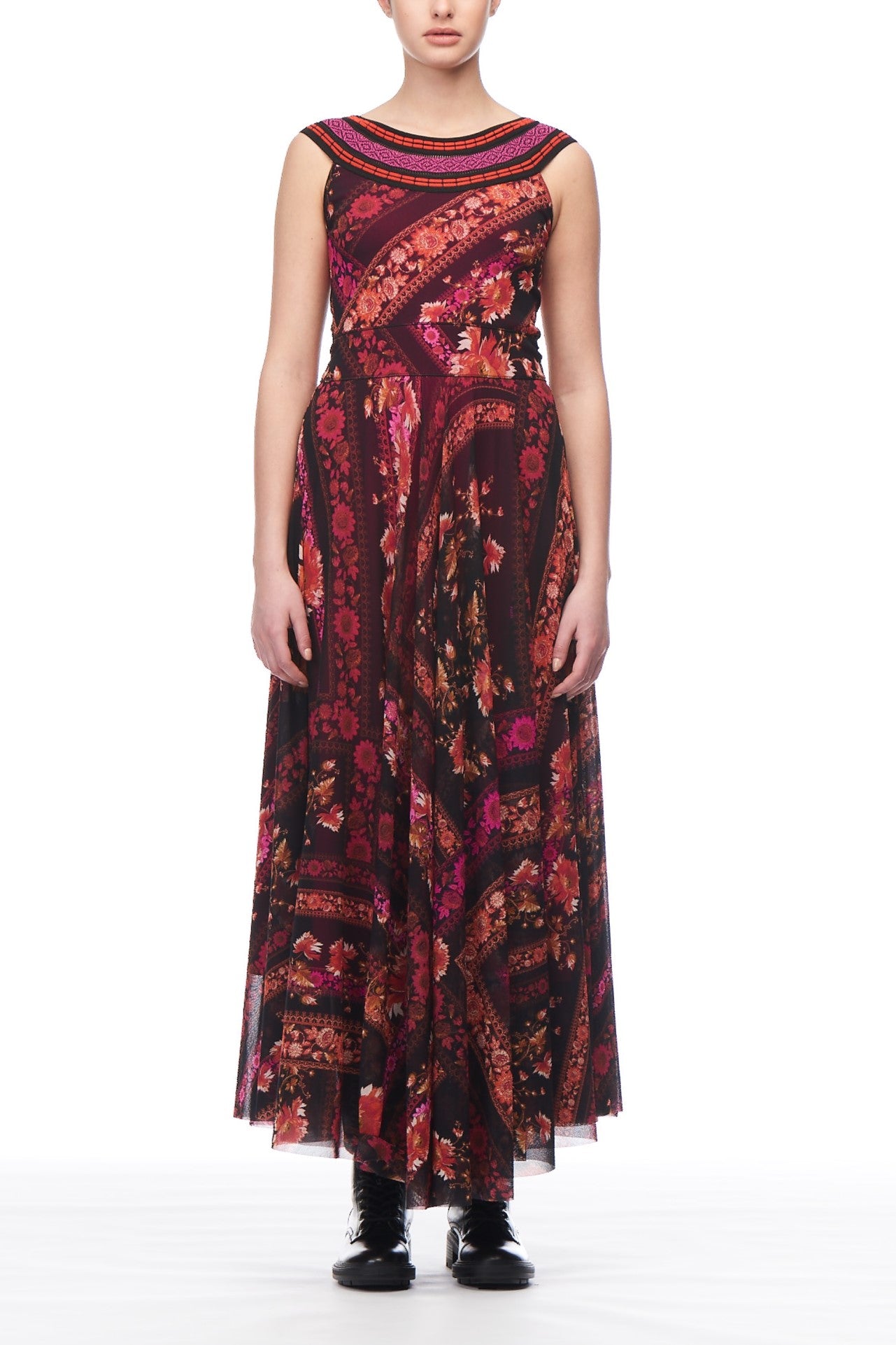 A person wearing the Fuzzi Woman Boho-Chic Floral Maxi Dress by Fuzzi, which features a sleeveless, floor-length design with a vibrant red, pink, and orange floral print, stands against a white background. They complement the look with black boots.