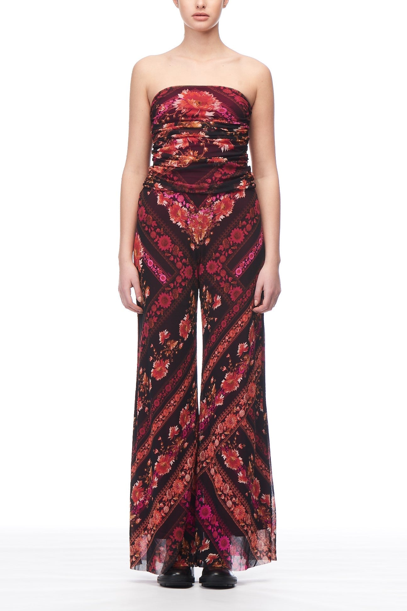 A person is dressed in a Fuzzi Woman Boho-Chic Jumpsuit by Fuzzi, showcasing a vibrant floral print in shades of red, pink, and black. The outfit is characterized by its wide-leg pants, creating an effortlessly chic silhouette against a plain white background.