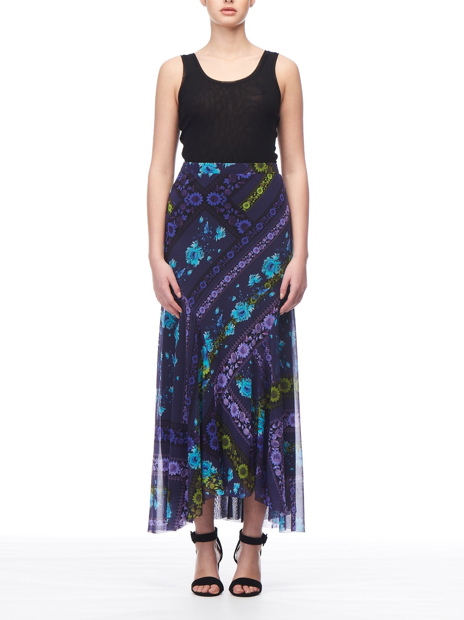 A person dressed in a sleeveless black top and the Fuzzi Woman Mesh Midi Skirt by Fuzzi, featuring a romantic colorful floral print, stands against a plain white background. They are wearing black high-heeled sandals.