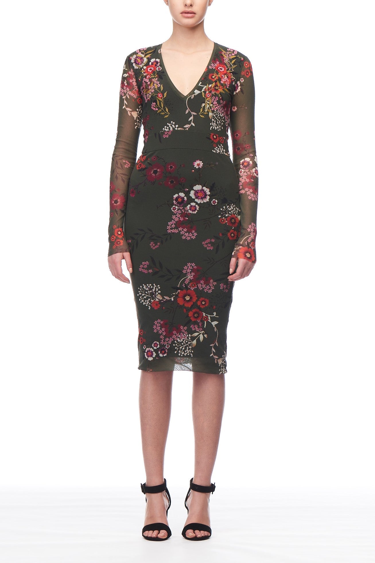 A person is wearing the Fuzzi Woman Intricate Floral Mesh Dress, a fitted, long-sleeve piece in olive green with a floral print. This vintage Fuzzi dress features a V-neckline and falls just below the knee. They complete the look with black high-heeled sandals.