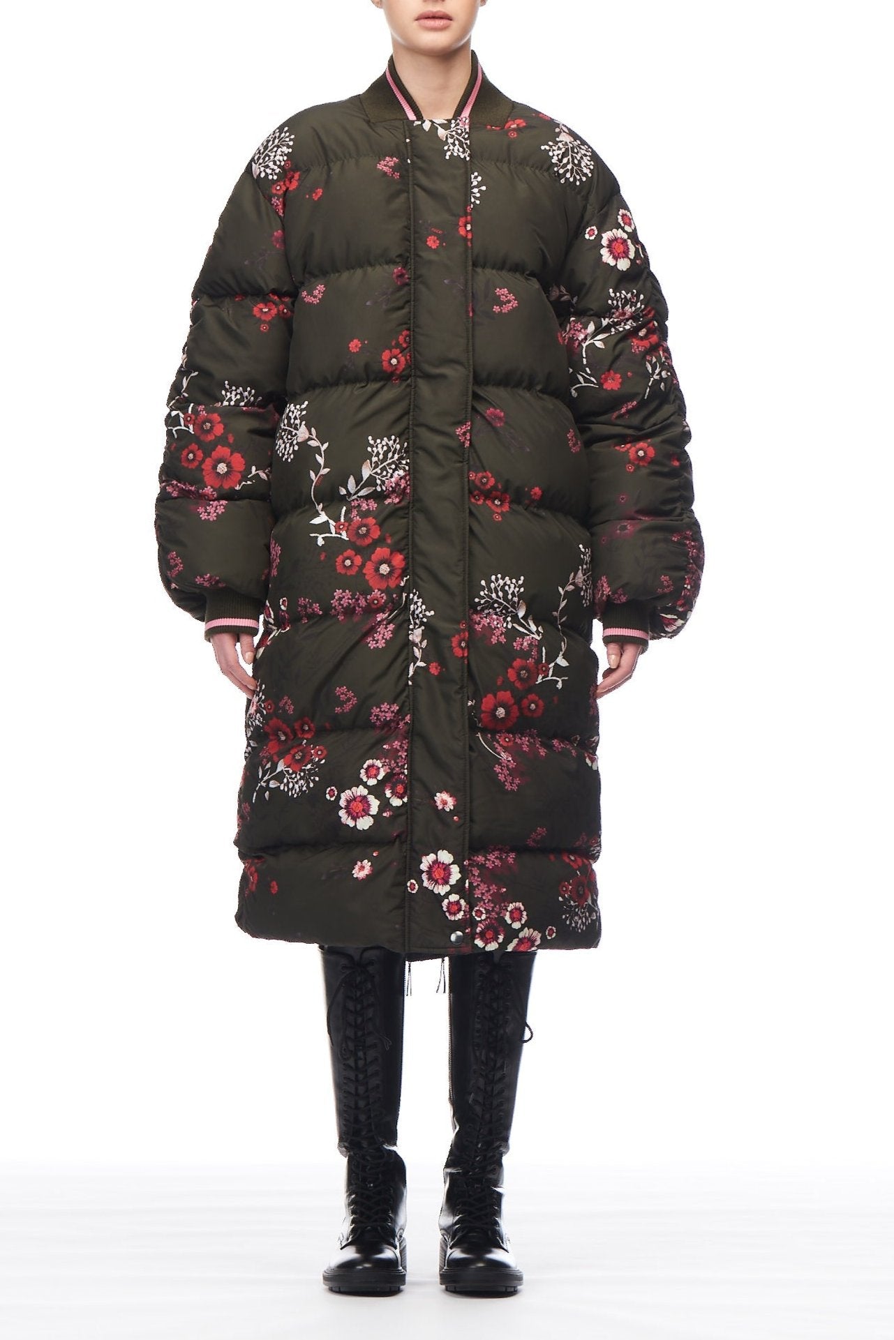 A person stands wearing the Fuzzi Woman Floral Puffer Coat, with its striking red and white floral print, making it an ideal choice for the winter season. The coat is complemented by black lace-up boots. The white background accentuates the ensemble beautifully.